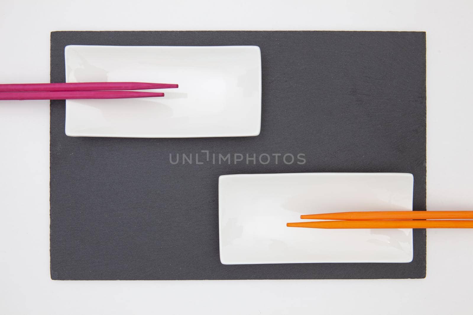 Rectangular slate plate with ceramic plate purple and orange chopsticks for sushi on the white table.  by CaptureLight