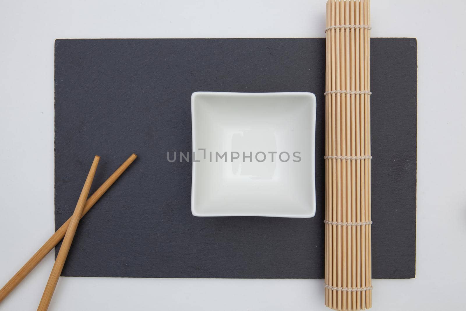 Rectangular slate plate with chopsticks, ceramic plate, bamboo mat for sushi on the white table.