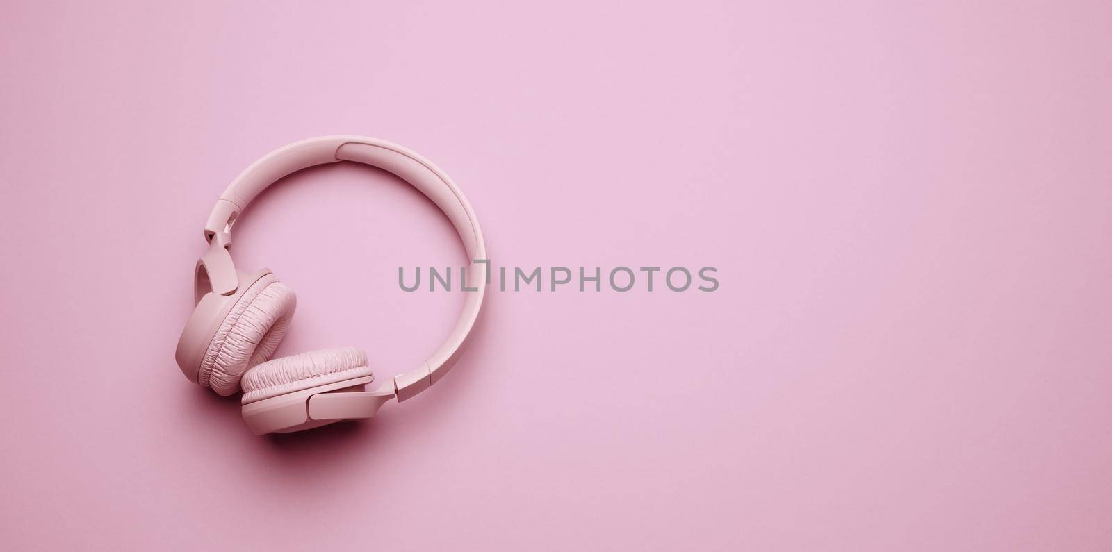 pink wireless headphones on a pink background, banner. Top view on modern gadget, place for an inscription