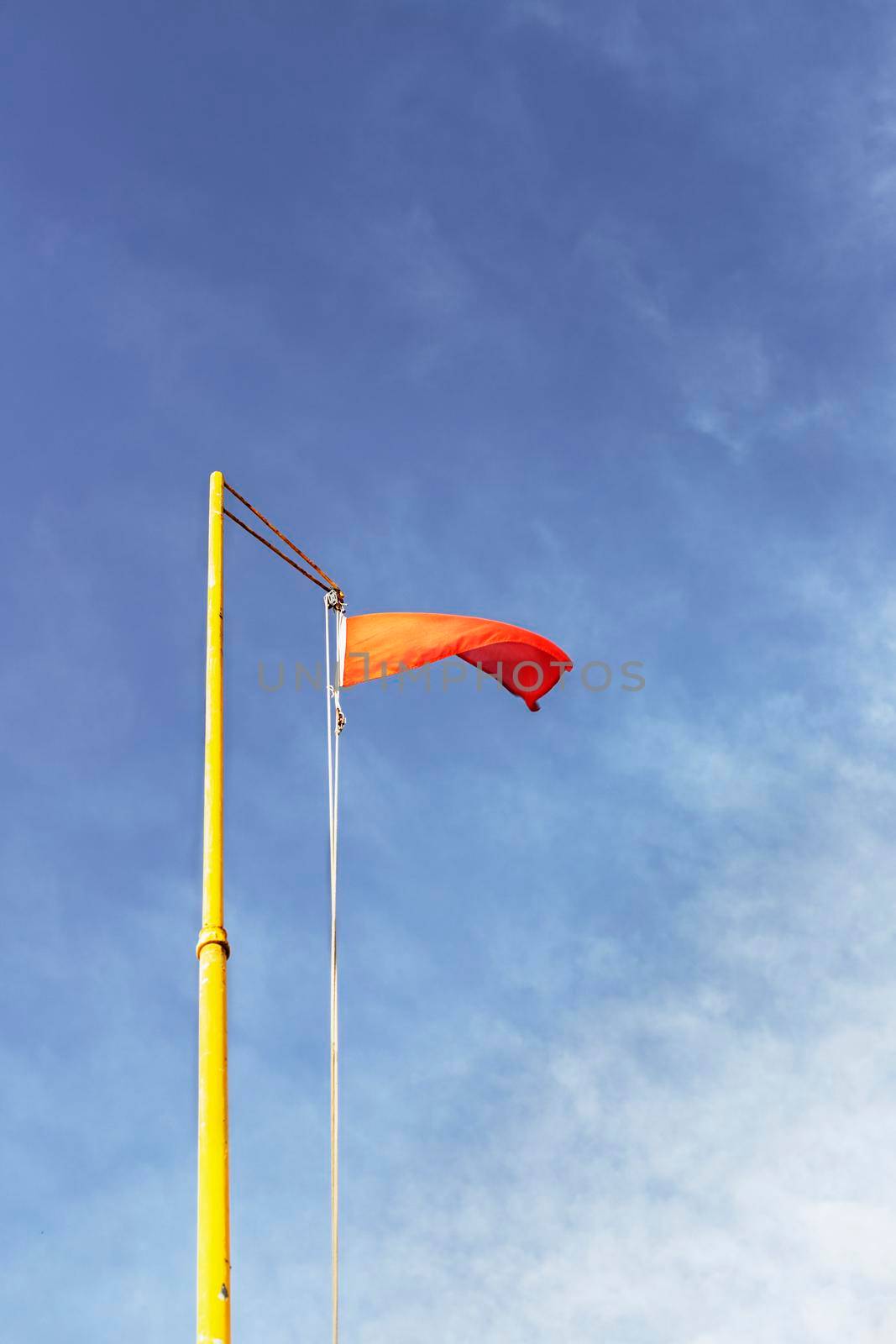 Red warning flag on a yellow flagpole against a blue and cloudy sky  seen from below