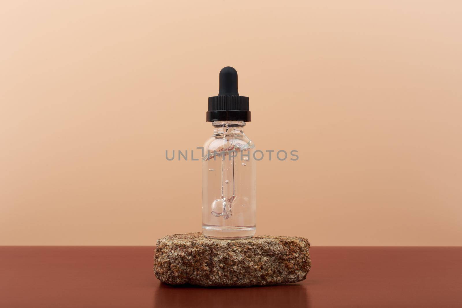 Skin serum in transparent bottle with black cap on a stone and brown table against beige background with copy space. Concept of skin treatment and beauty products to cure acne