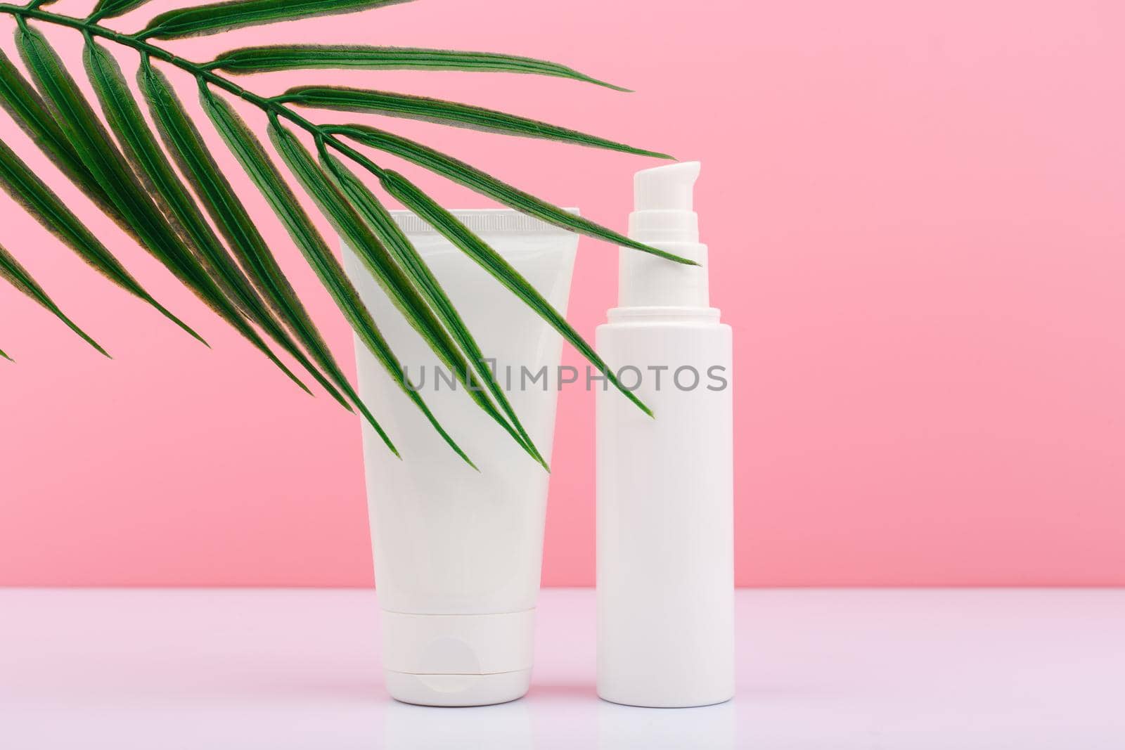 Two white unbranded cream tubes against pink background with palm leaf by Senorina_Irina