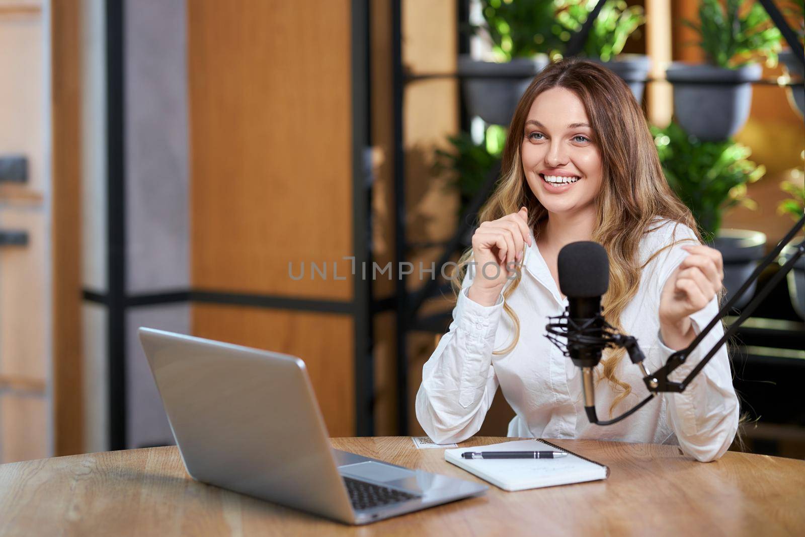 Close up portrait of happy young beautiful woman in white shirt talking about different topics with followers online by laptop. Concept of interview or live broadcast for subscribers. 