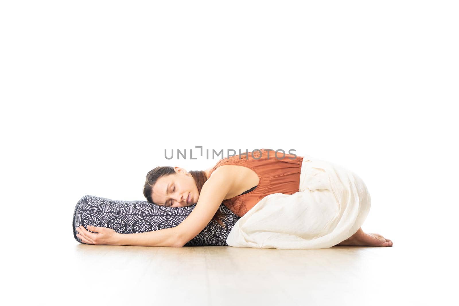 Restorative yoga with a bolster. Young sporty attractive woman in bright white yoga studio, lying on bolster cushion, stretching and relaxing during restorative yoga. Healthy active lifestyle by kasto