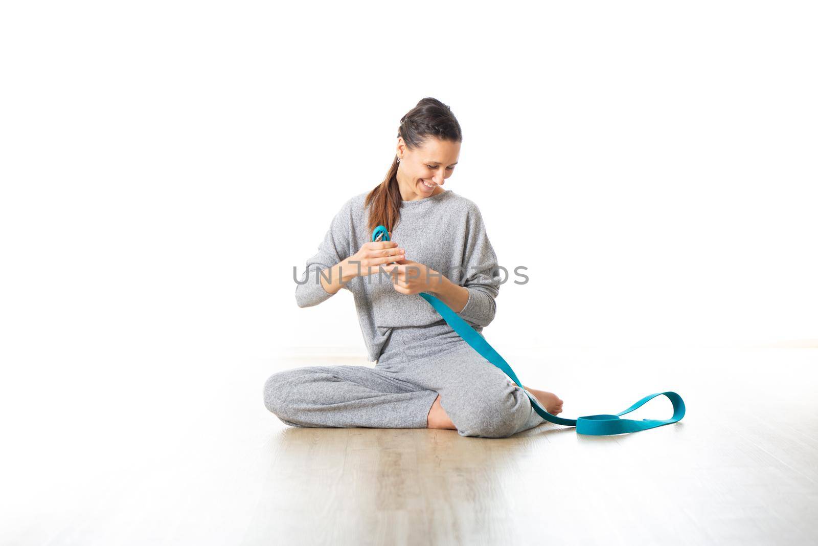 Young sporty female yoga instructor in bright white yoga studio, smiling cheerfully while preparing yoga exercise props.