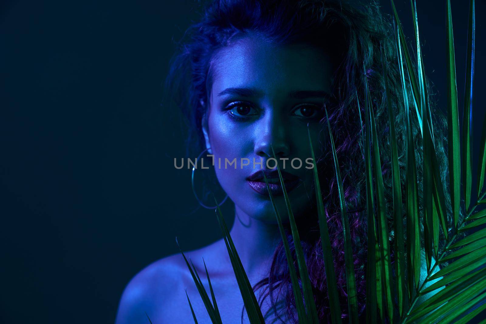 Fashion portrait of atrractive woman with modern green leaf accssesoies in professional studion with special dark blue lights. Concept of famous model on professional photo shoot. 