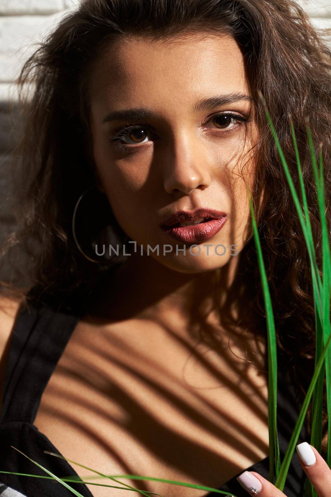 Portrait of attractive brunette young woman with trendy makeup posing with green leaves in sensual mood. Concept of professional photo shoot in a good atmosphere. 