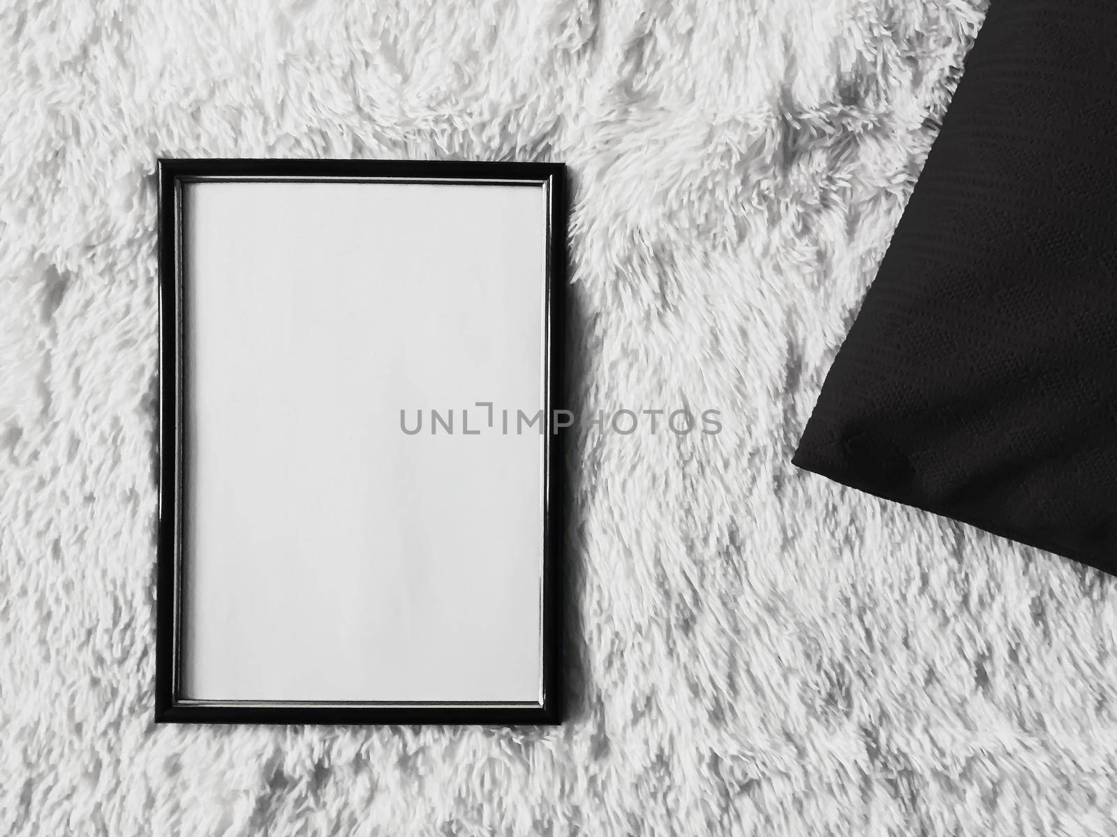 Thin wooden frame with blank copyspace as poster photo print mockup, black cushion pillow and fluffy white blanket, flat lay background and art product, top view