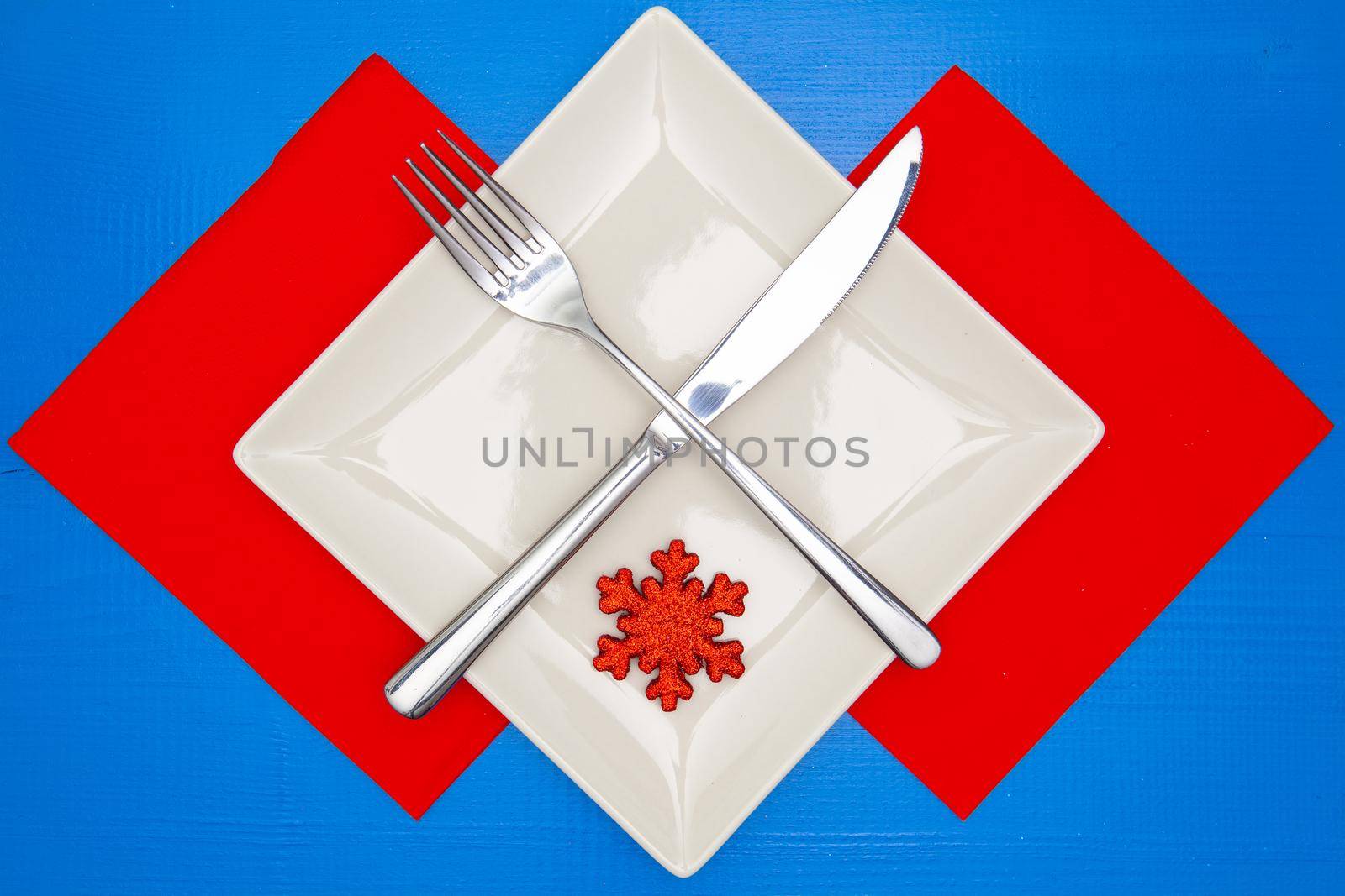 White square plate and red Christmas decoration on the blue wooden table.Top view.Flat Lay Image.
