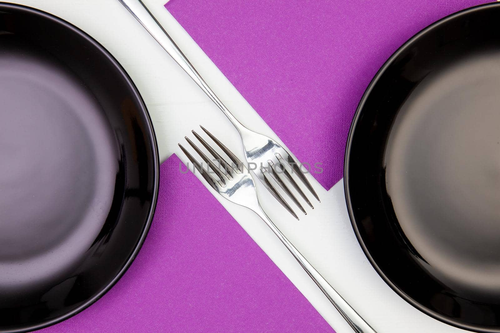 Black plates and purple napkins on the white wooden table.Top view. Flat Lay Image.