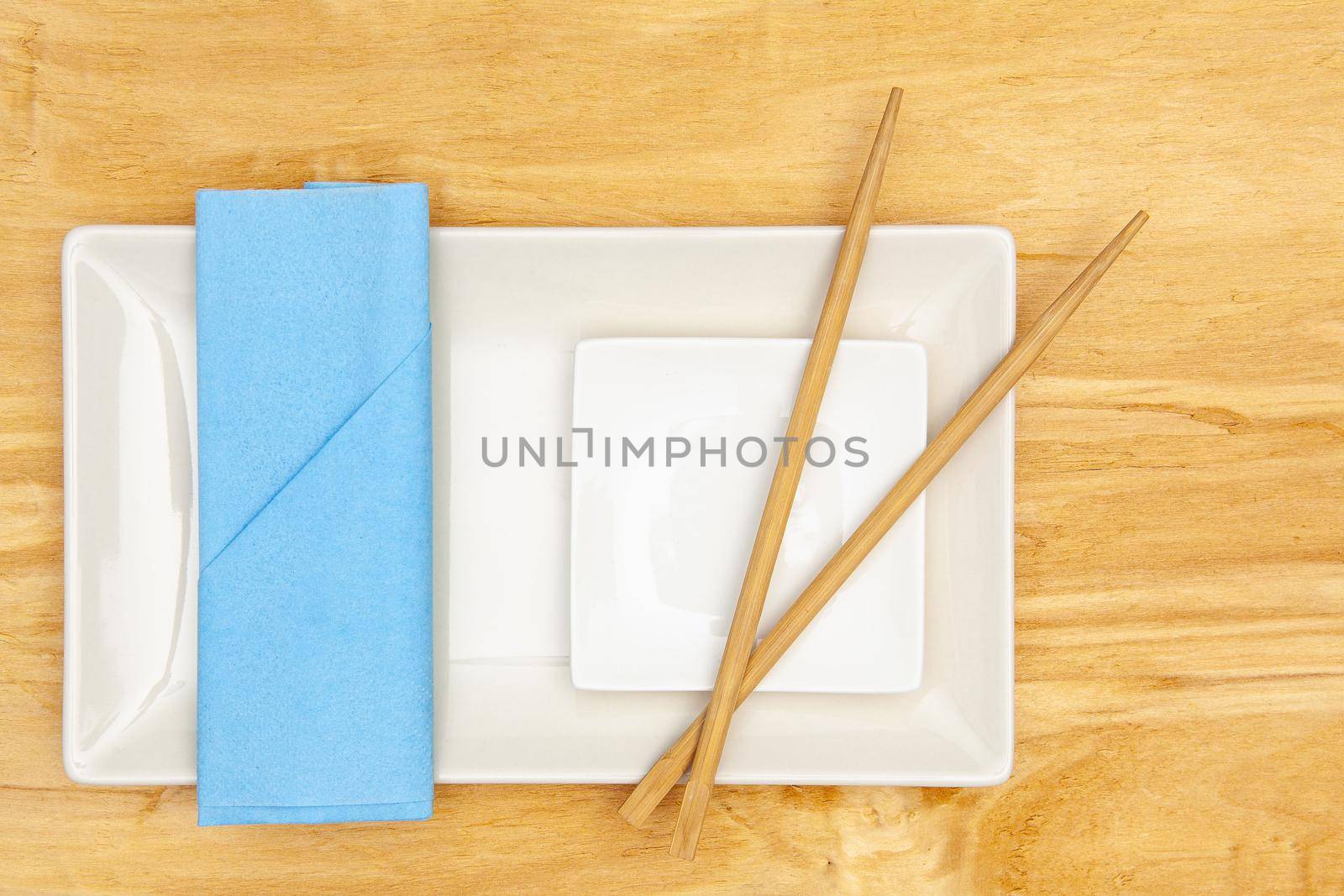 Ceramic bowls  and bamboo chopsticks for sushi food with blue napkin.