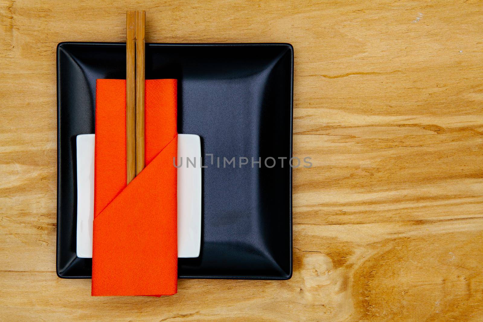 Black ceramic bowls  and bamboo chopsticks for sushi food with orange napkin.
