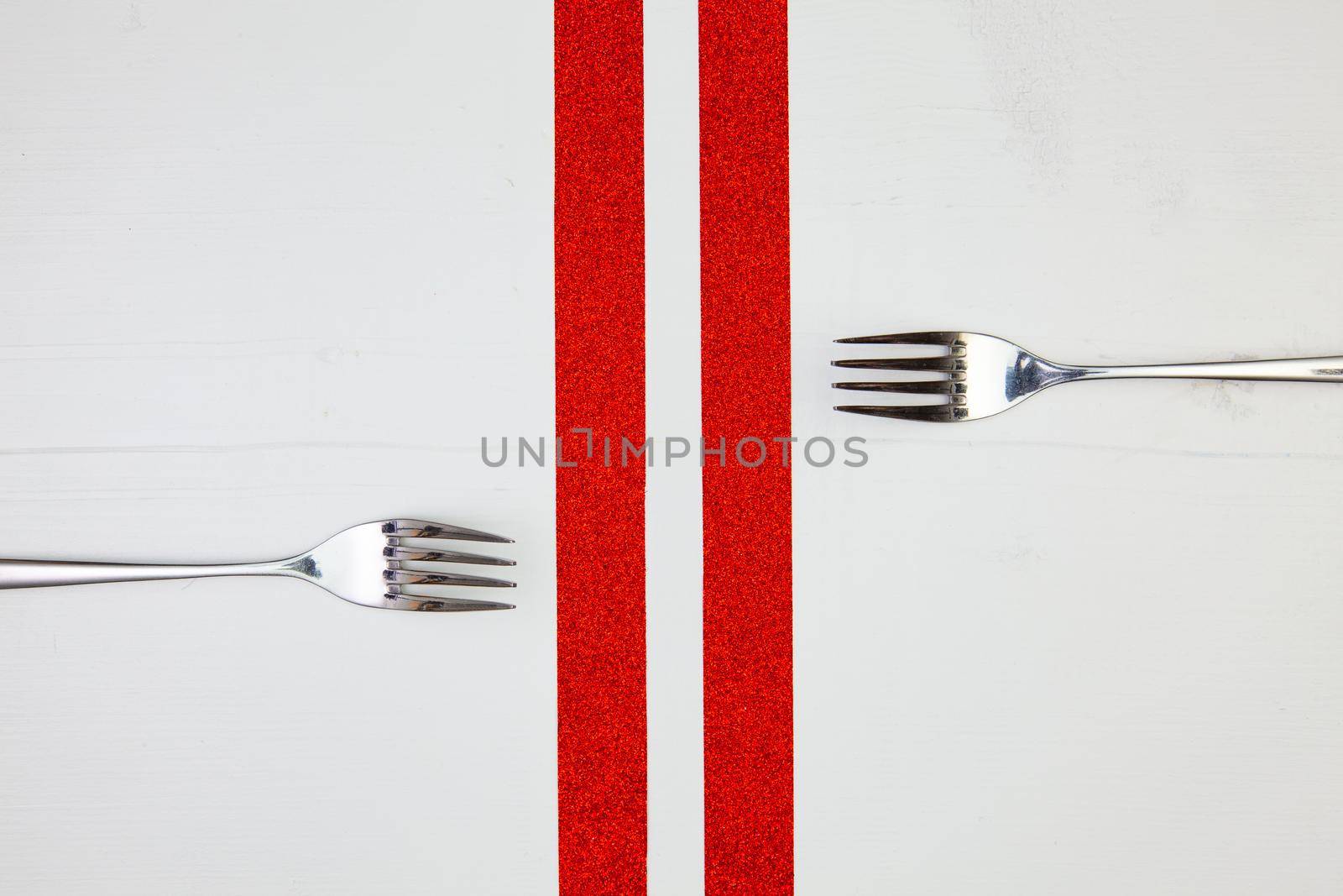 Two forks and red ribbons on the wooden table.