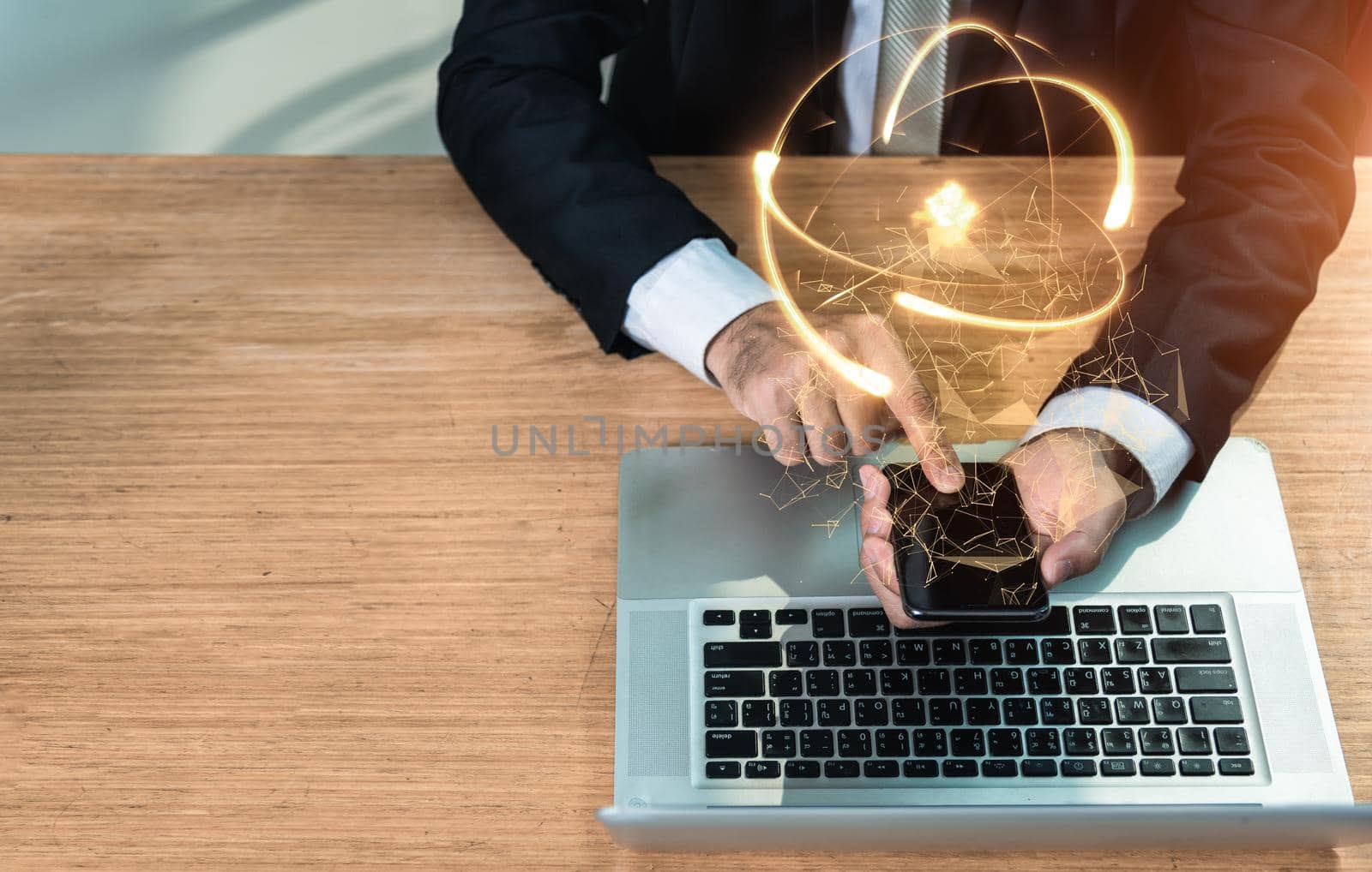 Businessman working on smartphone with social network diagram at front laptop computer on wooden desk