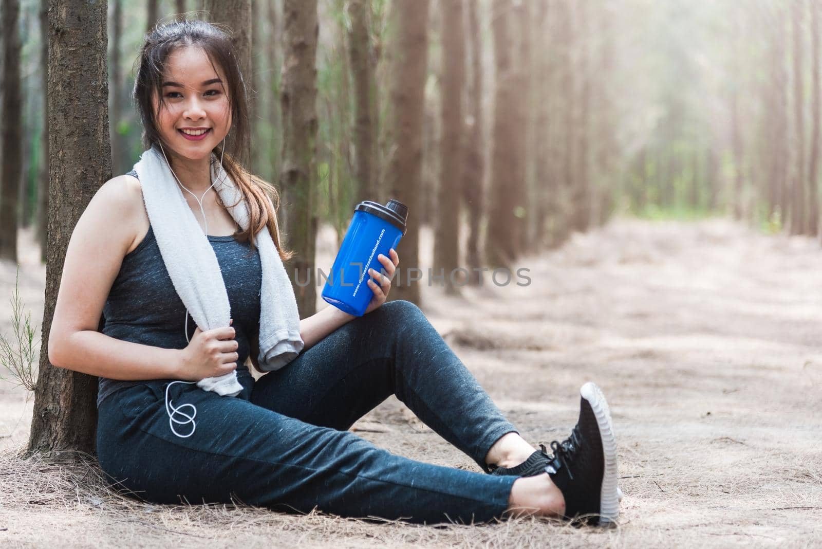 Beautiful sport young woman girl lifestyle exercise healthy break drinking water from bottle after running workout in forest nature park with copy space