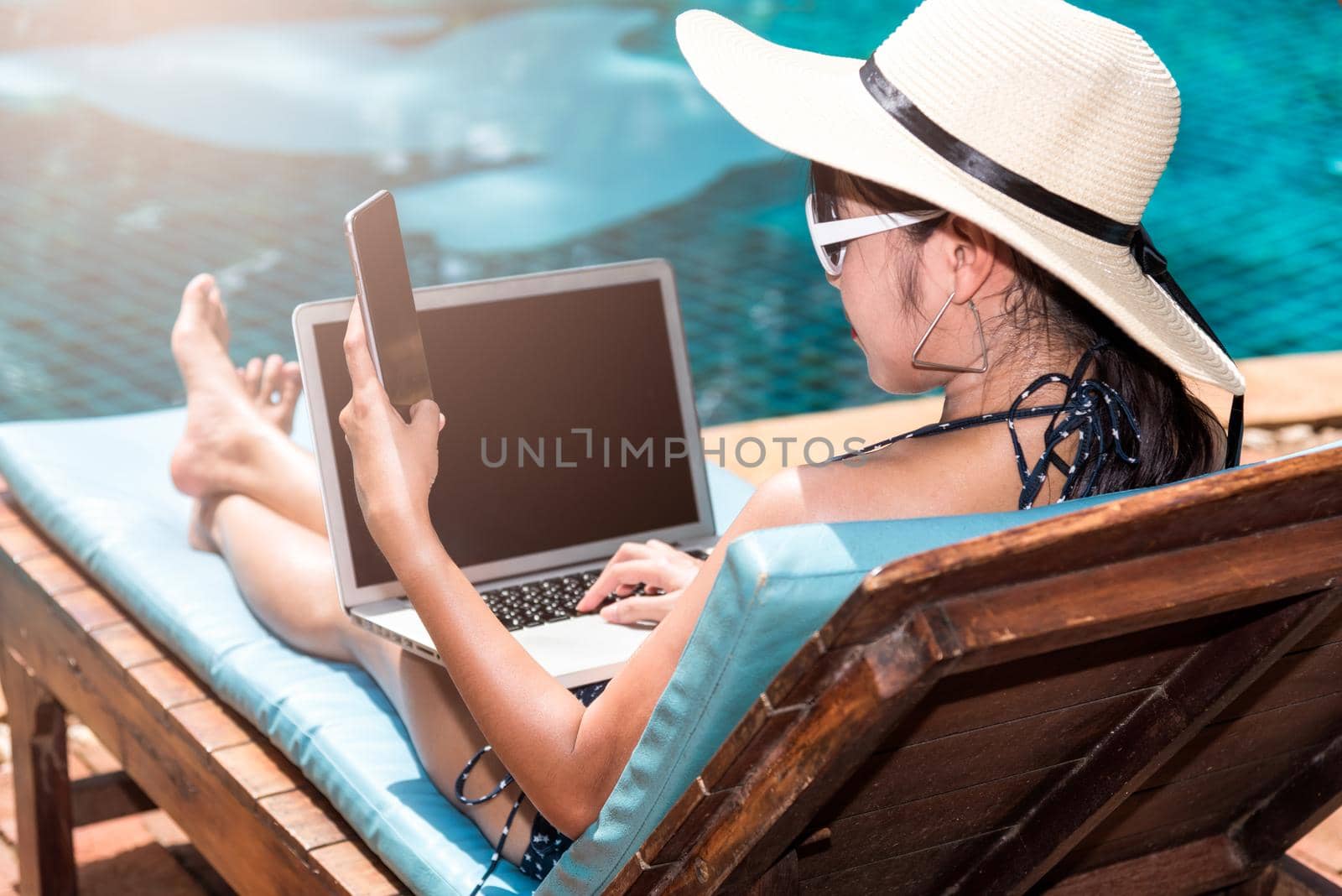 Portrait Beautiful Woman Sitting in deck chair and using laptop computer near swimming pool in vacation time by Sorapop