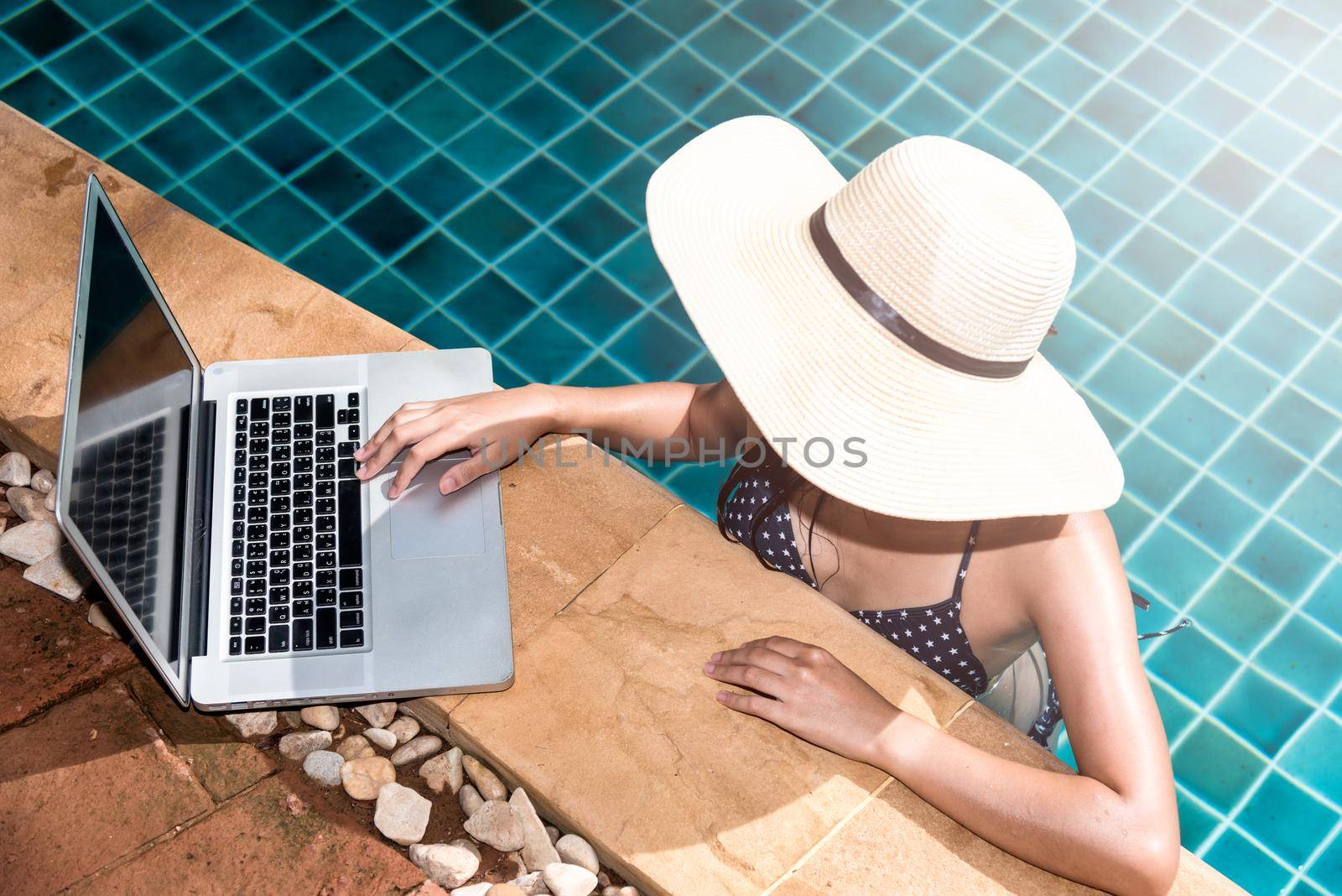 Beautiful smiling woman using laptop computer in swimming pool by Sorapop