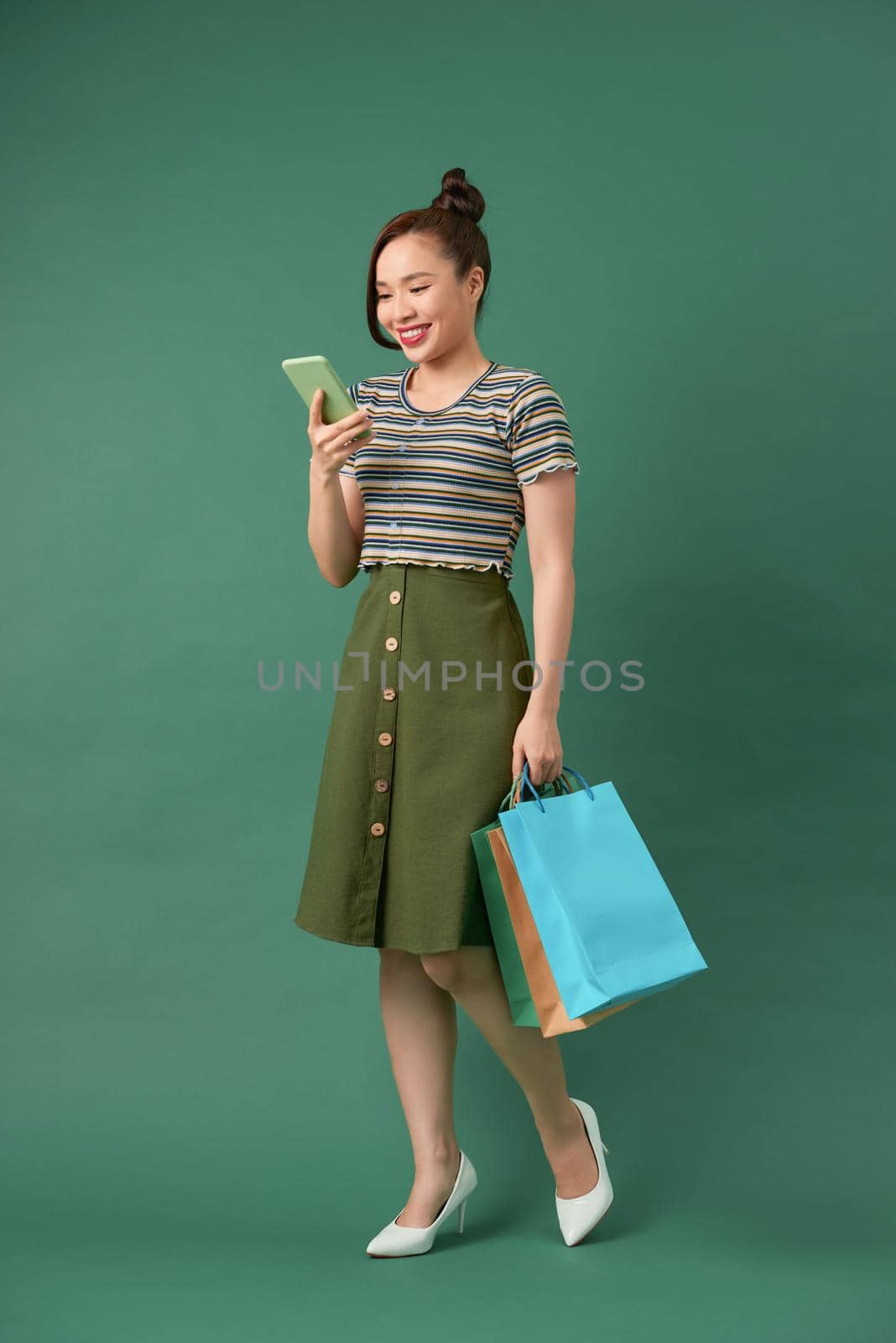 cheerful elegant girl holding shopping bags while chatting on smartphone on green background