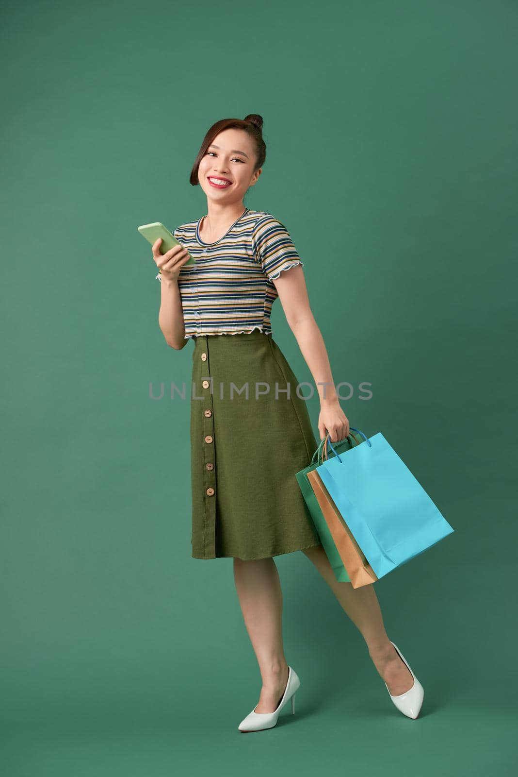 Full length portrait of a happy young woman holding shopping bags and mobile phone