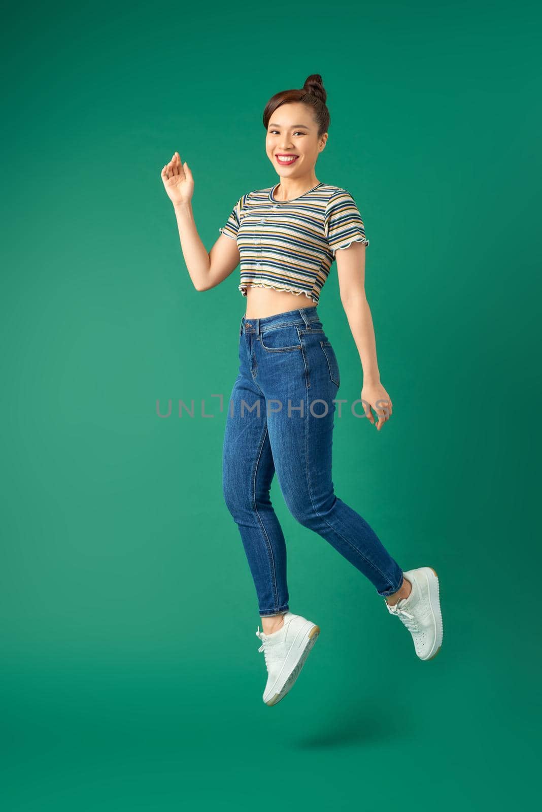 Happy carefree young woman jumping isolated over green background.