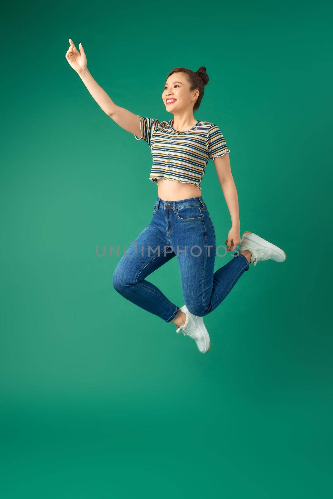 Happiness, freedom, motion and people concept - smiling young woman jumping in air over green background.