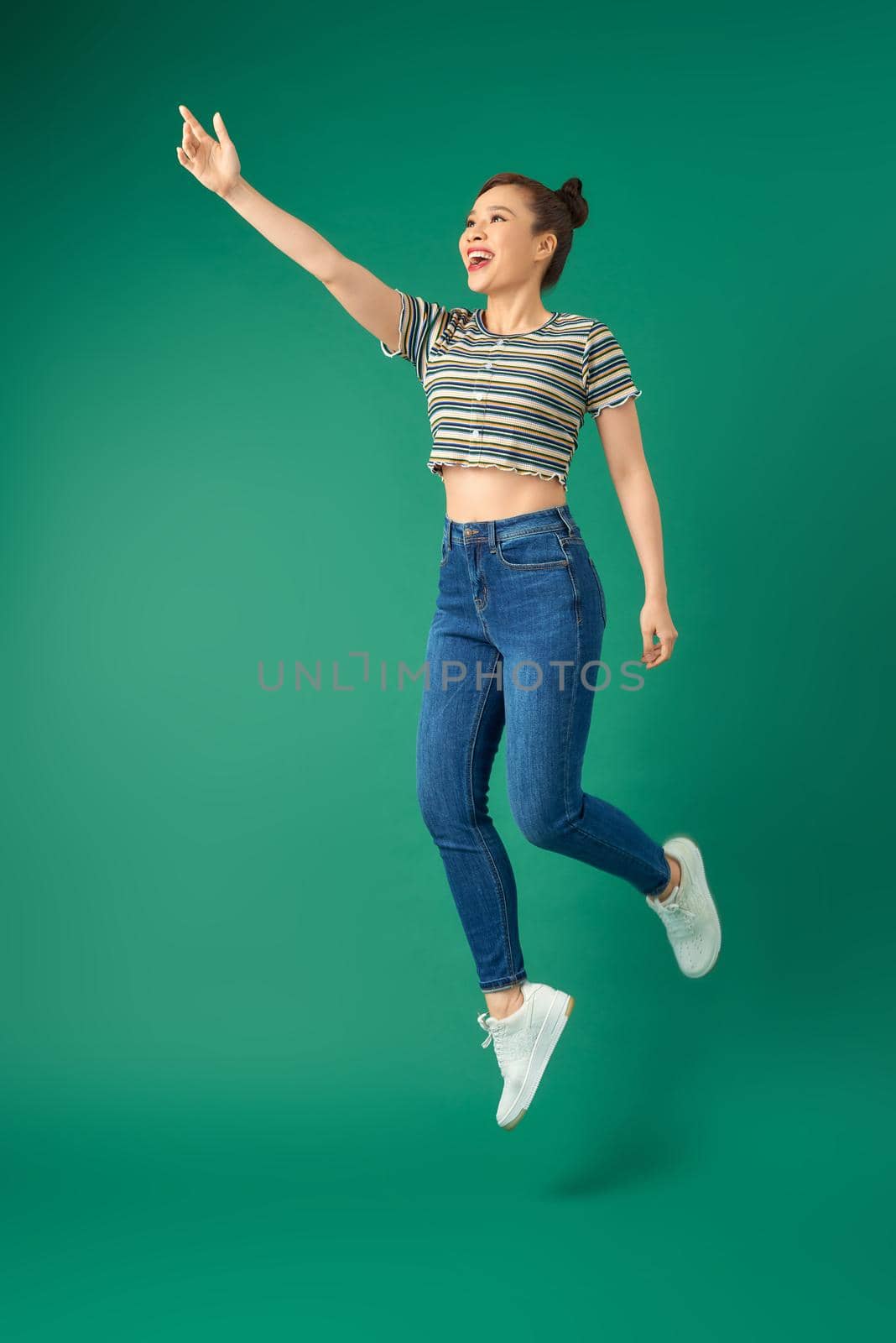 Full length of cheerful young Asian woman or teenage girl jumping in air over green background. by makidotvn