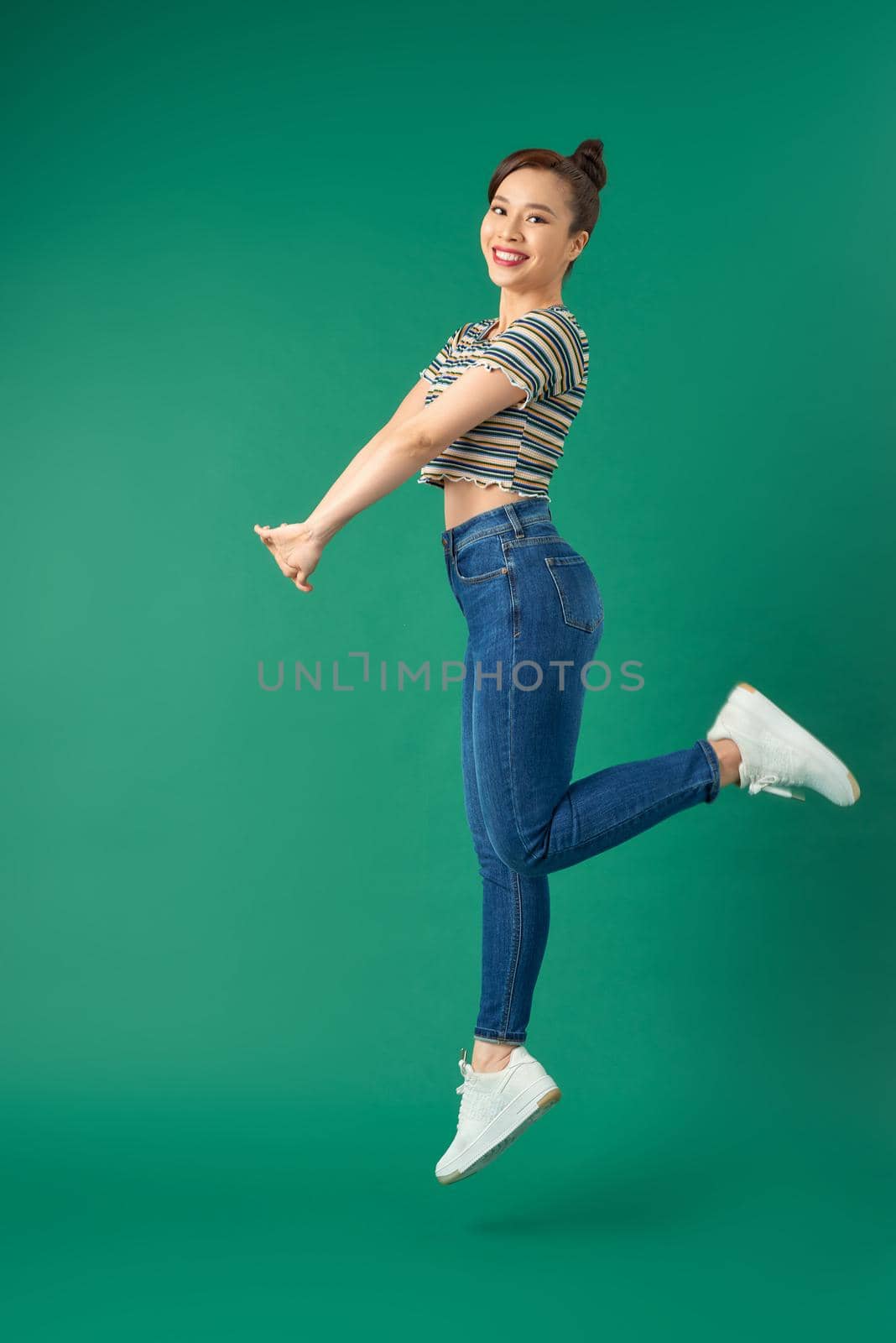 Full length of portrait of joyful young Asian woman jumping in air over green background.