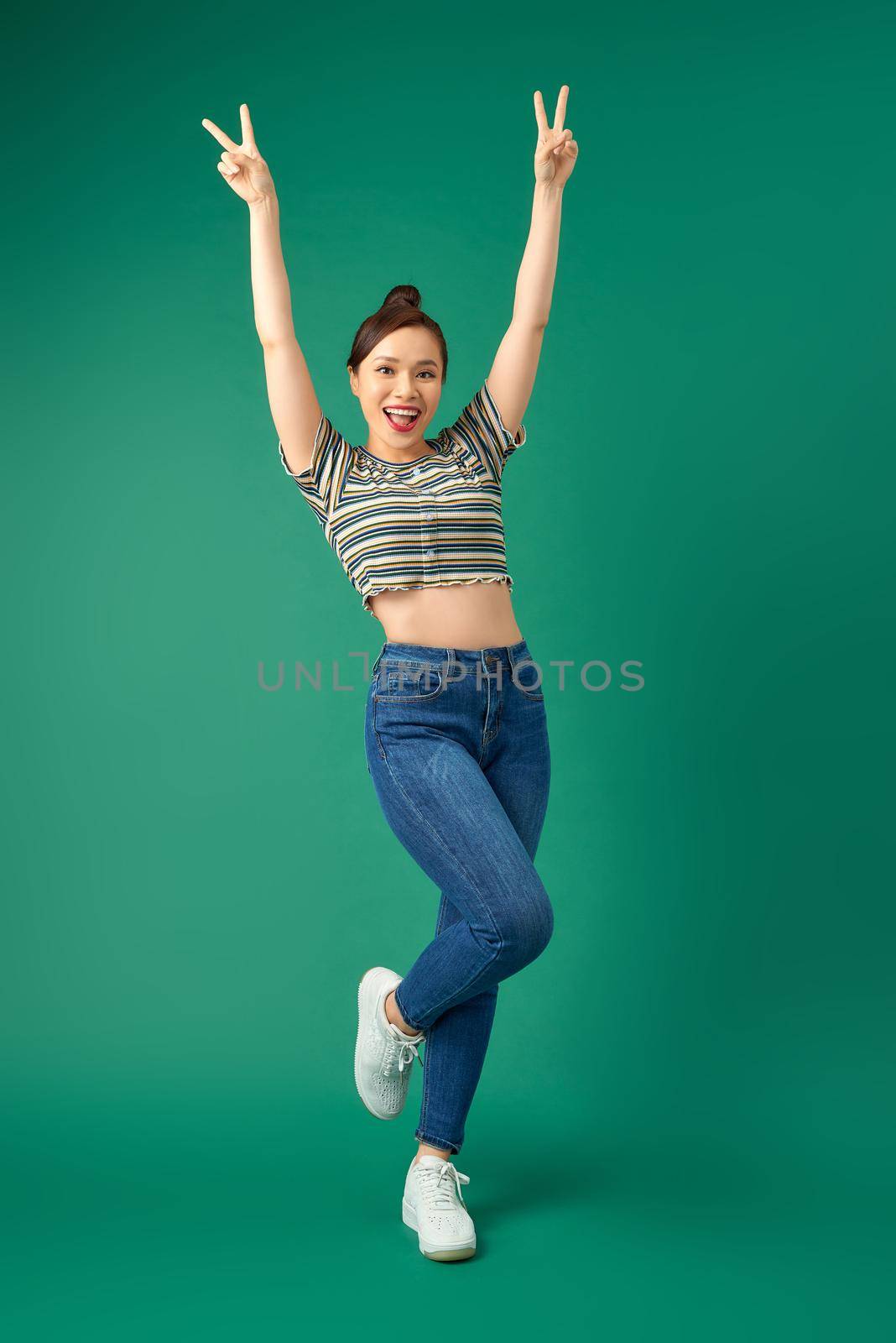 Full-length portrait of a joyful attractive Asian girl celebrating success while jumping over green background. by makidotvn