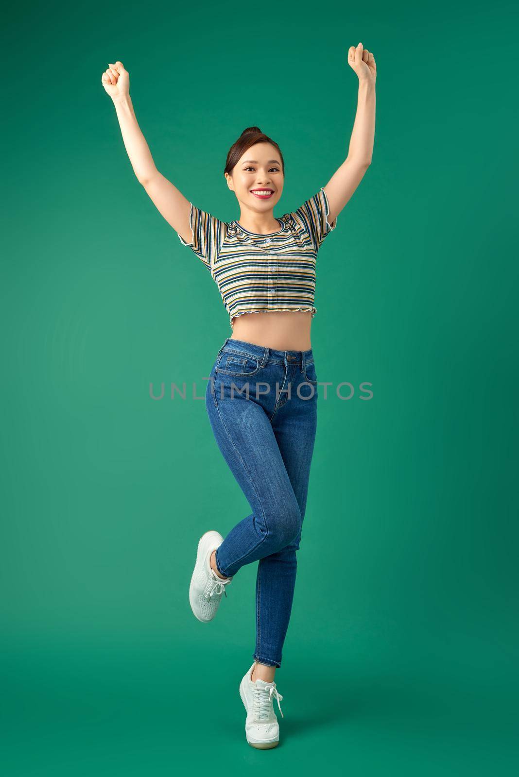 Full-length portrait of a joyful attractive Asian girl celebrating success while jumping over green background. by makidotvn