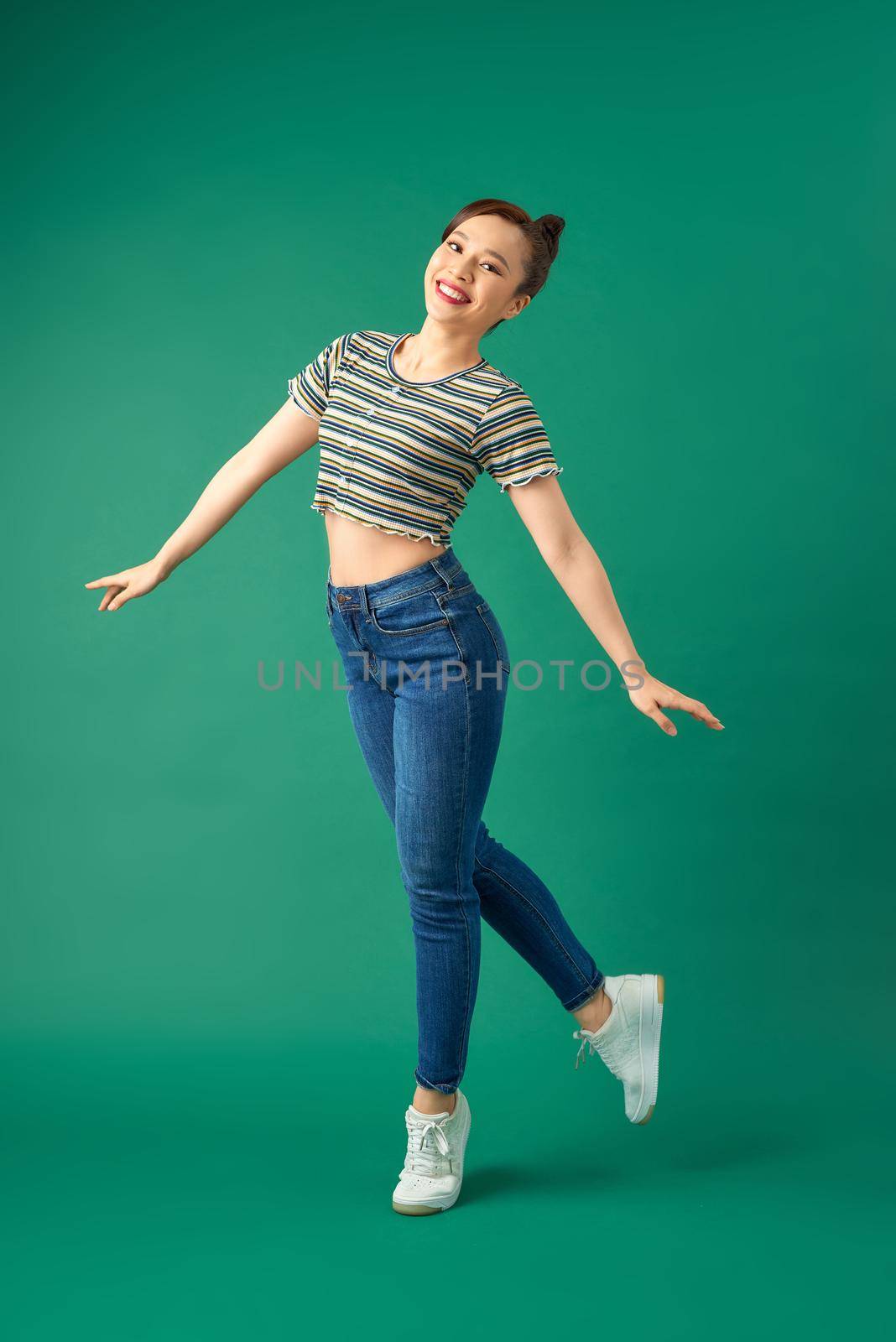 Full-length portrait of a joyful attractive Asian girl celebrating success while jumping over green background.