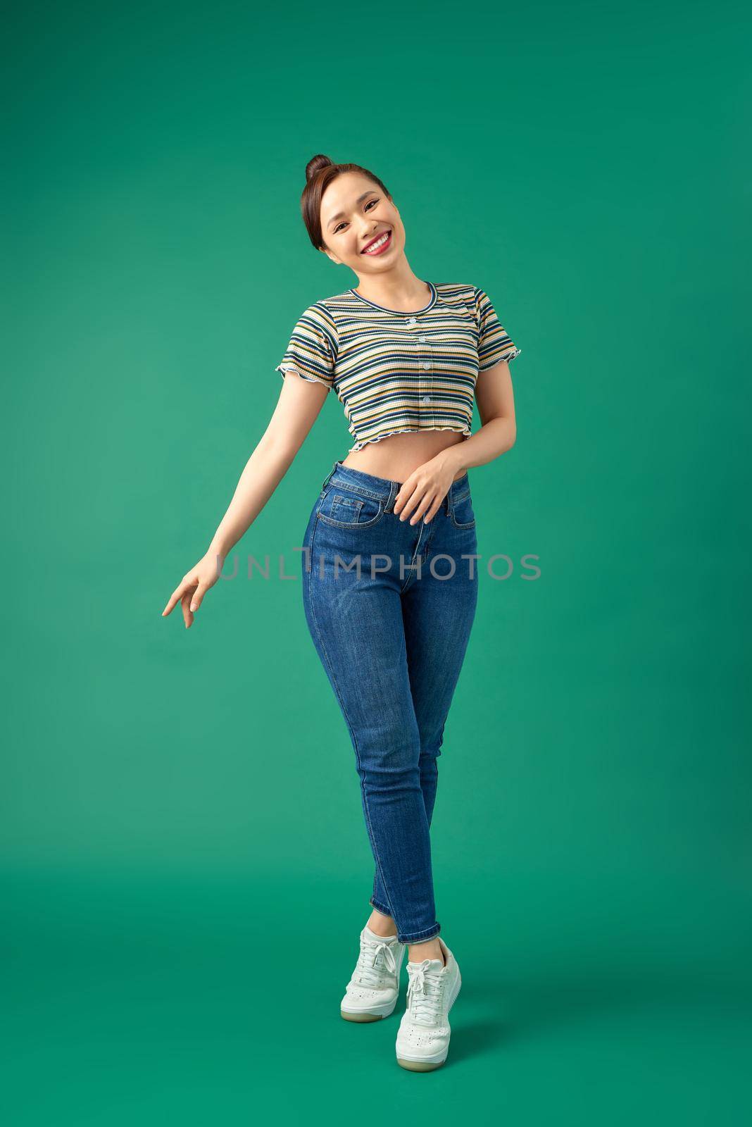 Full length image of beautiful Asian woman having fun and dancing isolated over green background