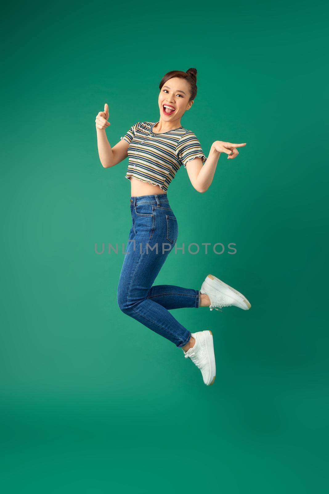 Portrait of happy positive young Asian woman jumping and waving hand over green background. by makidotvn