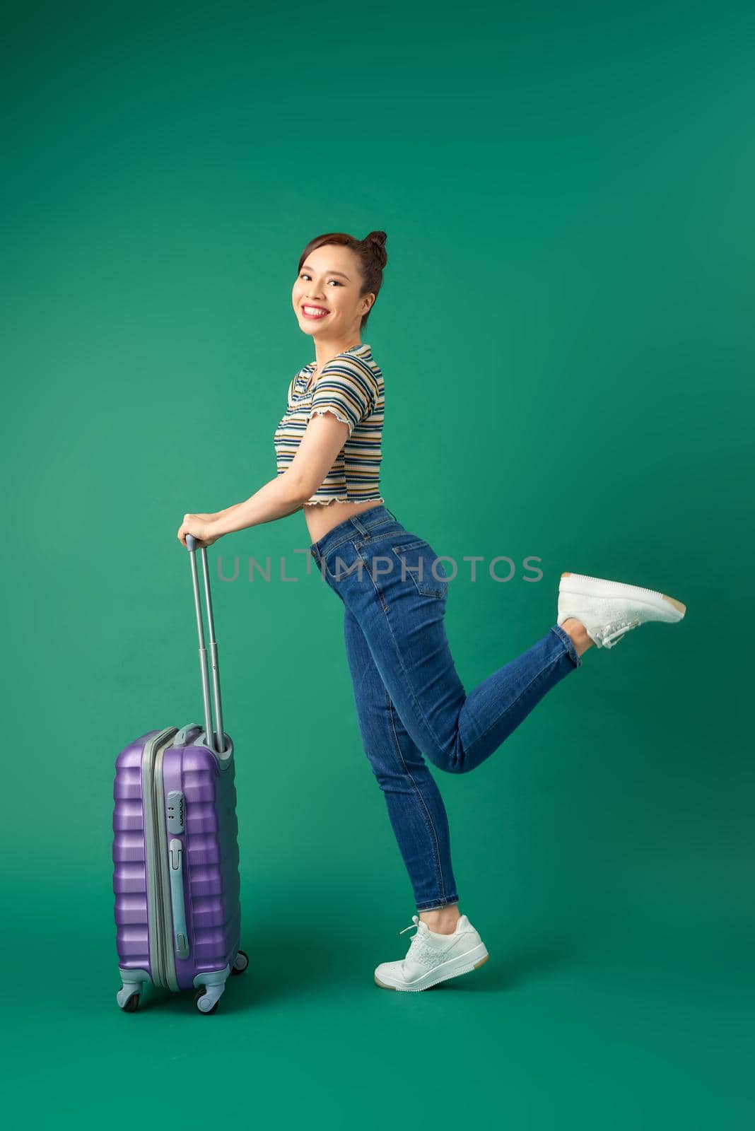 Carefree young Asian woman posing with suitcase isolated over green background. by makidotvn