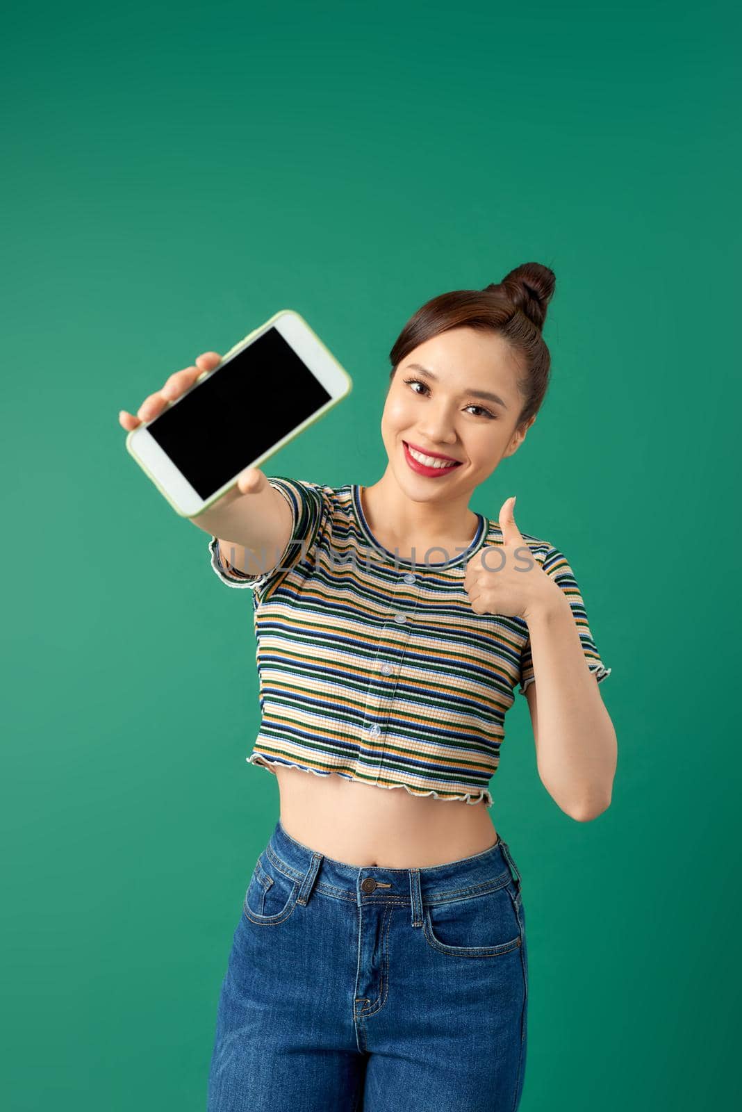 Close up portrait of a smiling Asian woman showing blank screen mobile phone over green background.