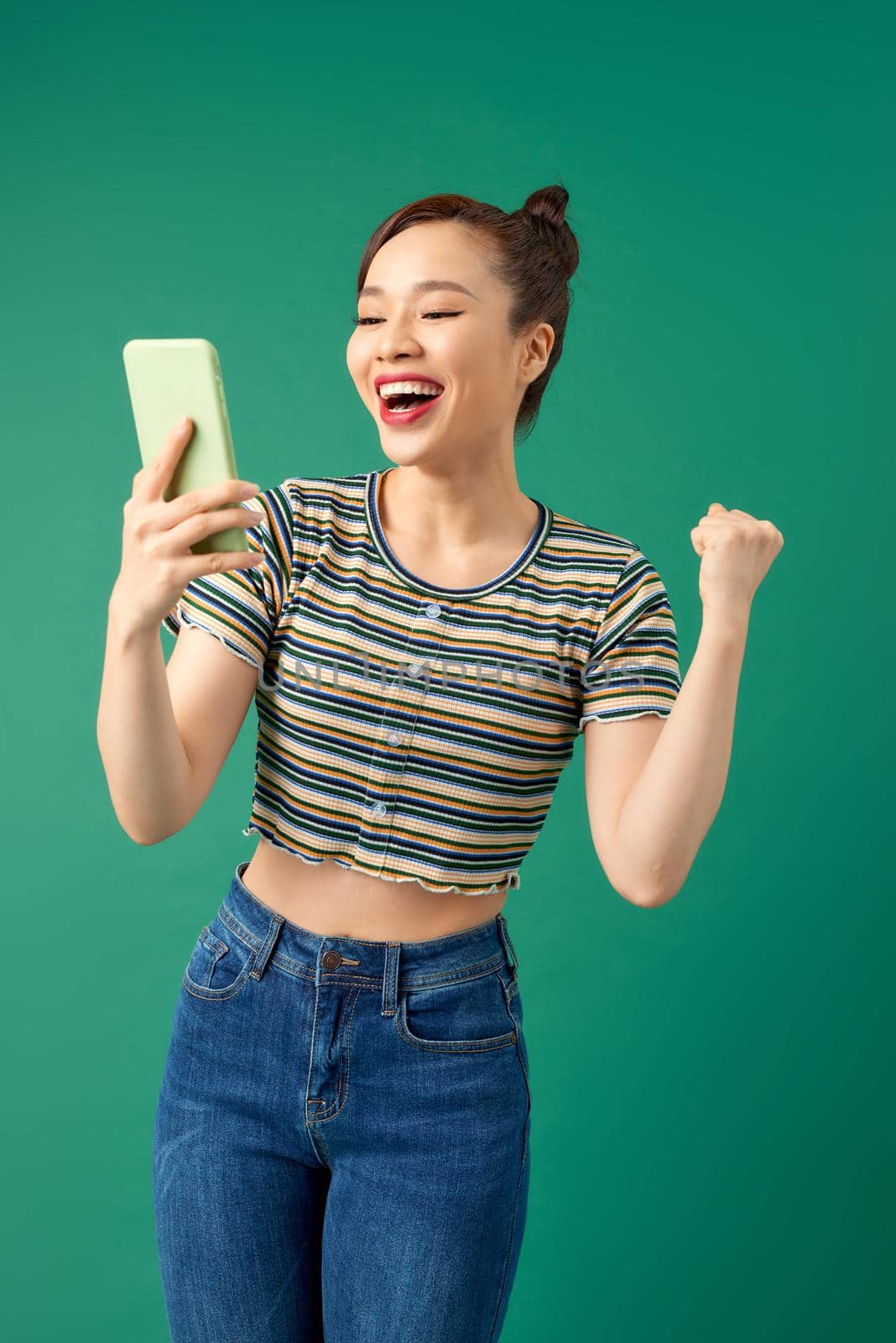 Portrait of a smiling woman making selfie photo on smartphone isolated on green background