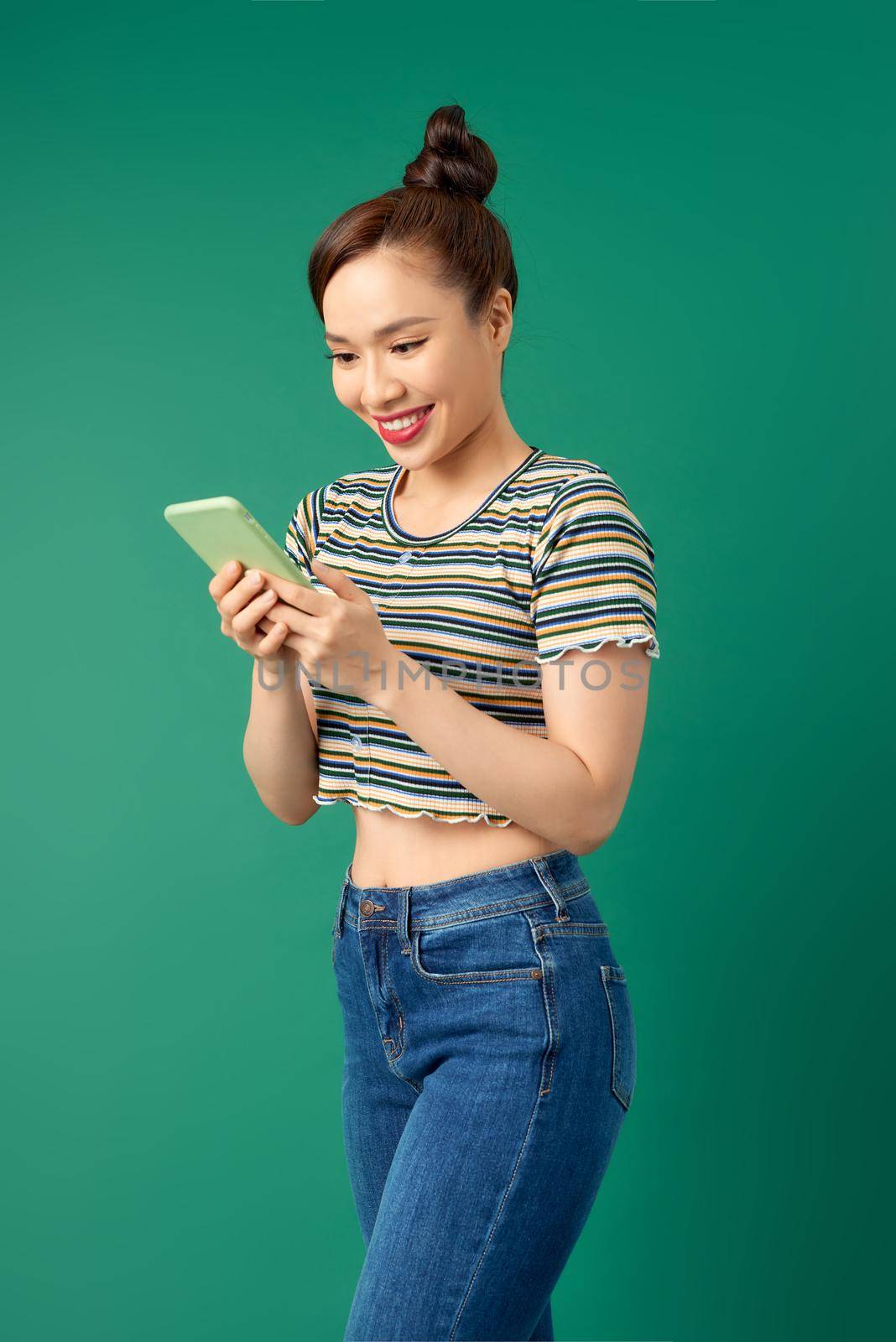 Smiling young Asian girl using smart phone isolated over green background.