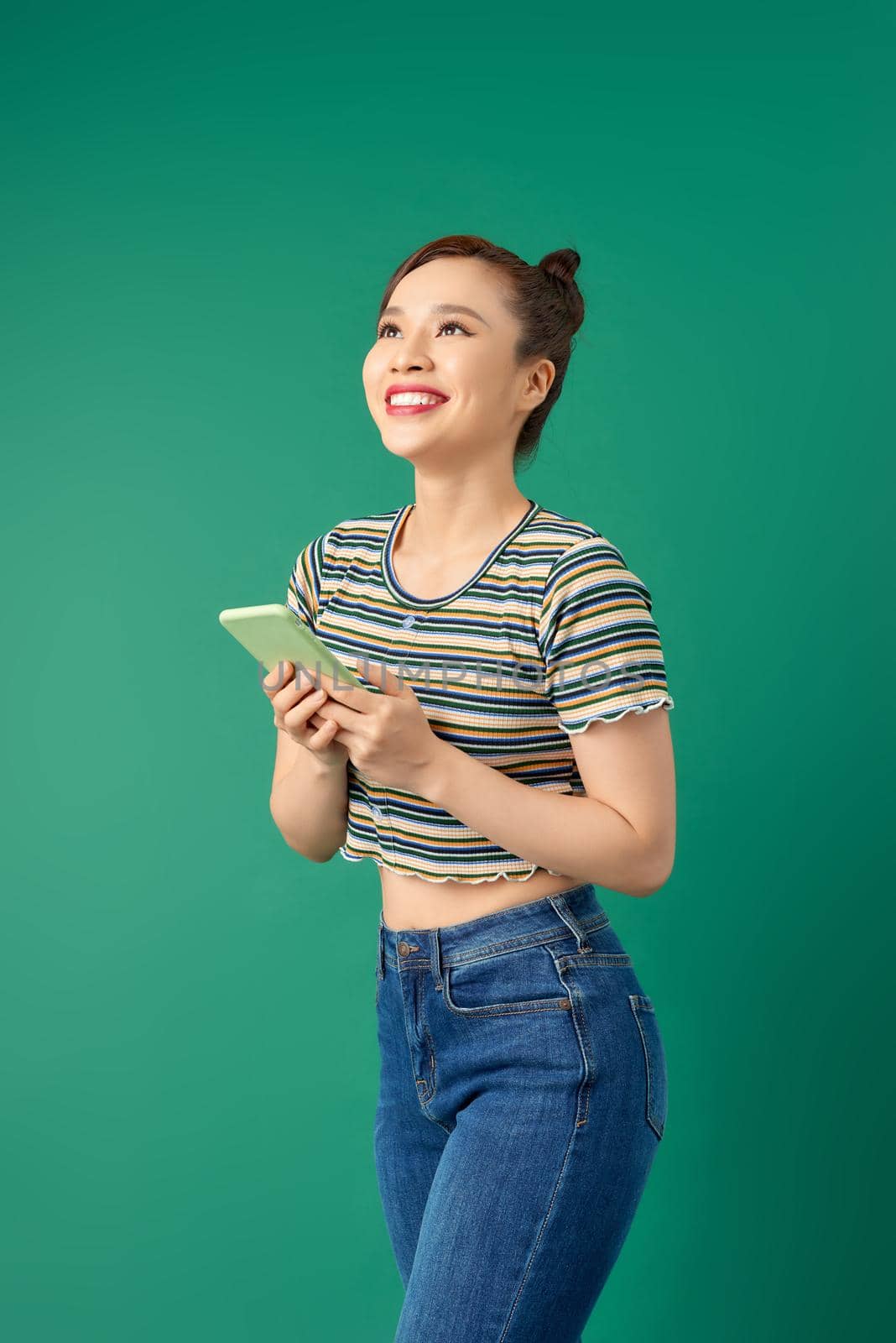 Pretty young Asian woman using smartphone in casual clothign over colorful green background
