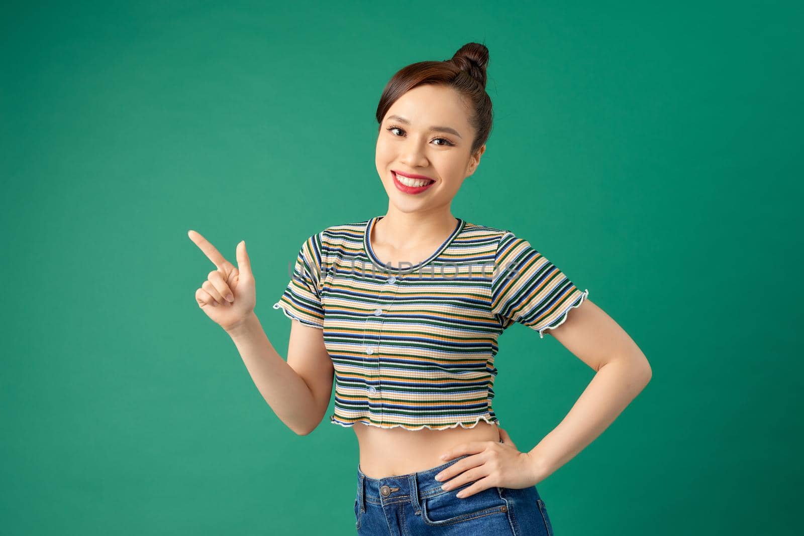Happy young Asian woman in casual clothing pointing her finger over green background.