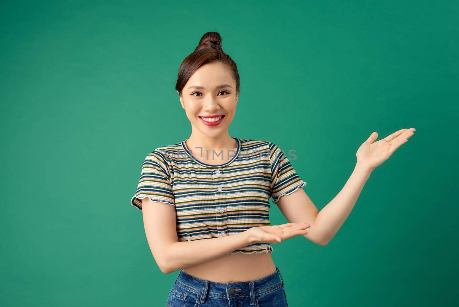 Happy smiling young Asian woman showing blank area for sign or copyspace, isolated over green background.