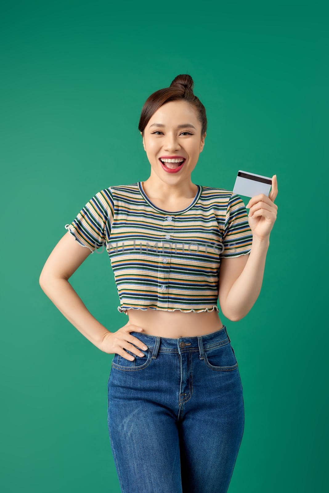 Portrait of smiling young Asian woman showing credit card over green background.
