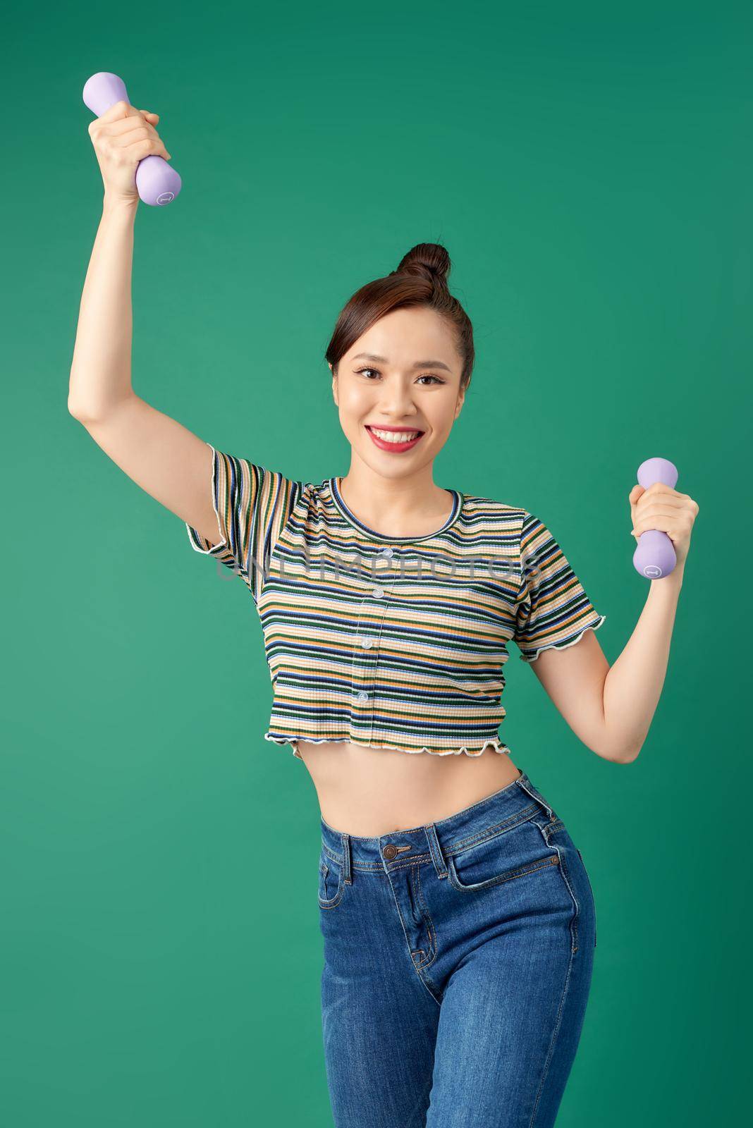 Smiling attractive young Asian woman practicing exercise with dumbell over green background. by makidotvn