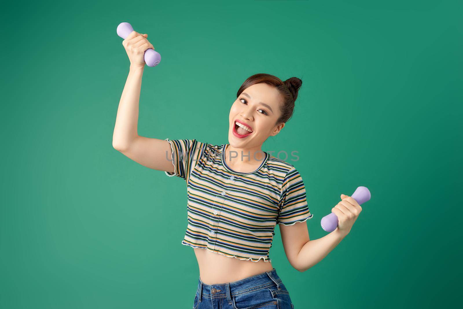 Young Asian woman holding dumbell and wearing casual clothing over green background. by makidotvn