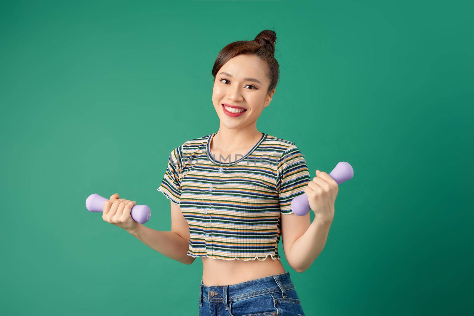 Young Asian woman holding dumbell and wearing casual clothing over green background.