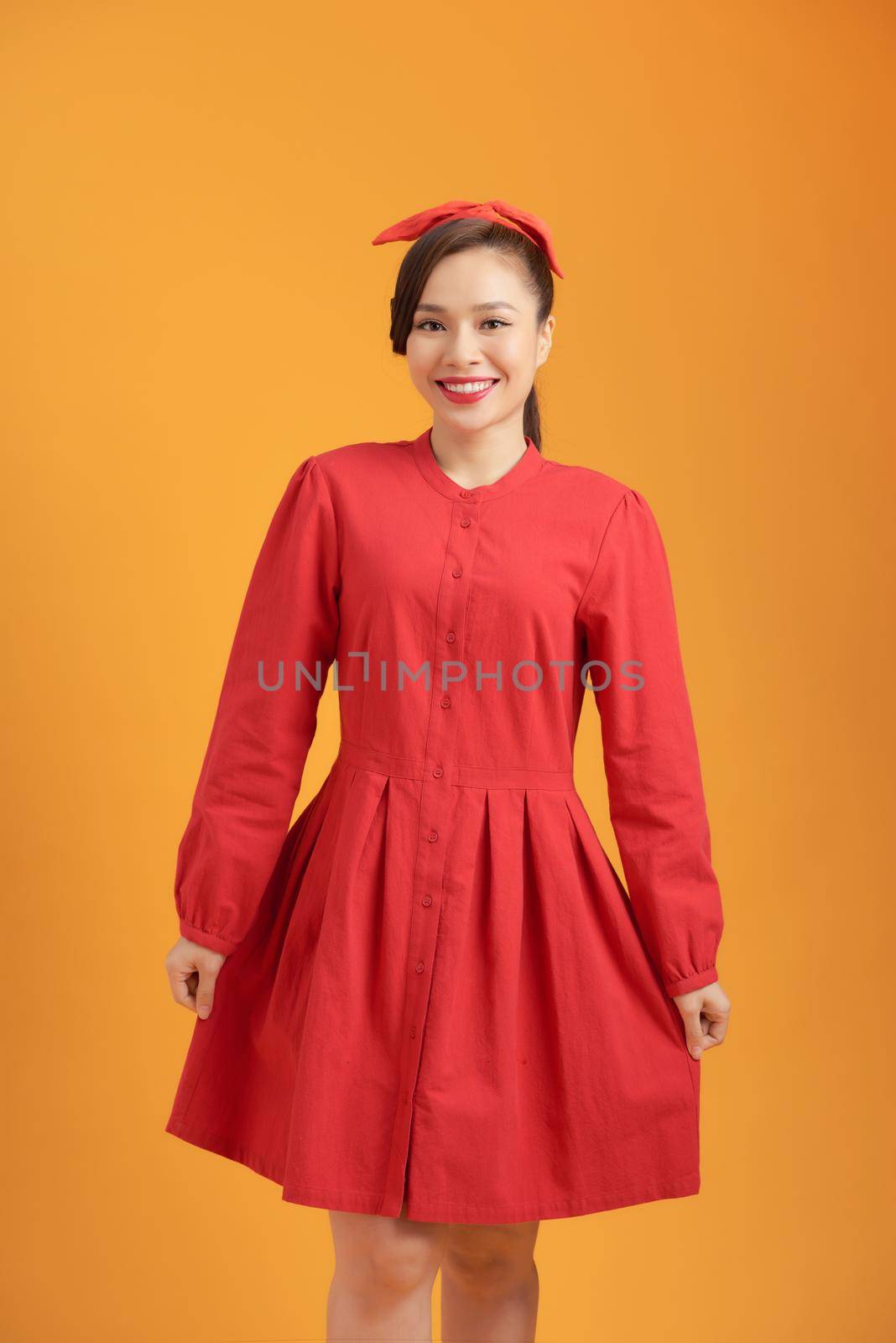 Full length of beautiful young Asian woman wearing red dress and standing over orange background by makidotvn