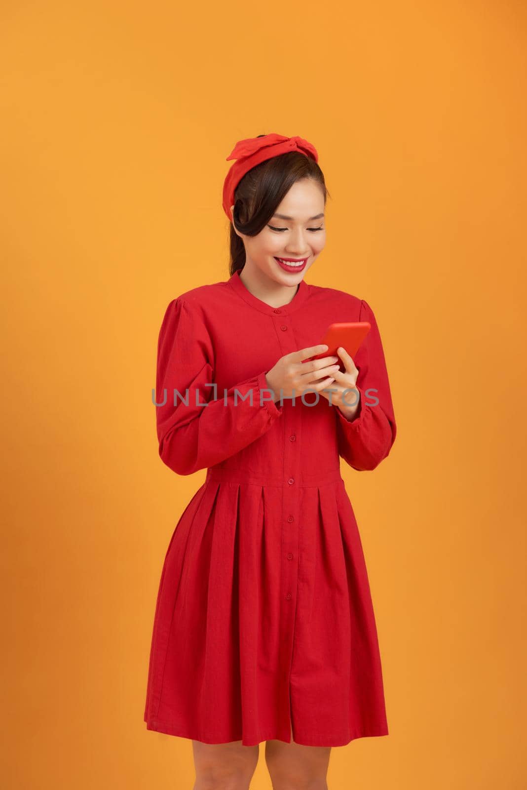 Portrait of happy young Asian woman using phone isolated over orange background. by makidotvn