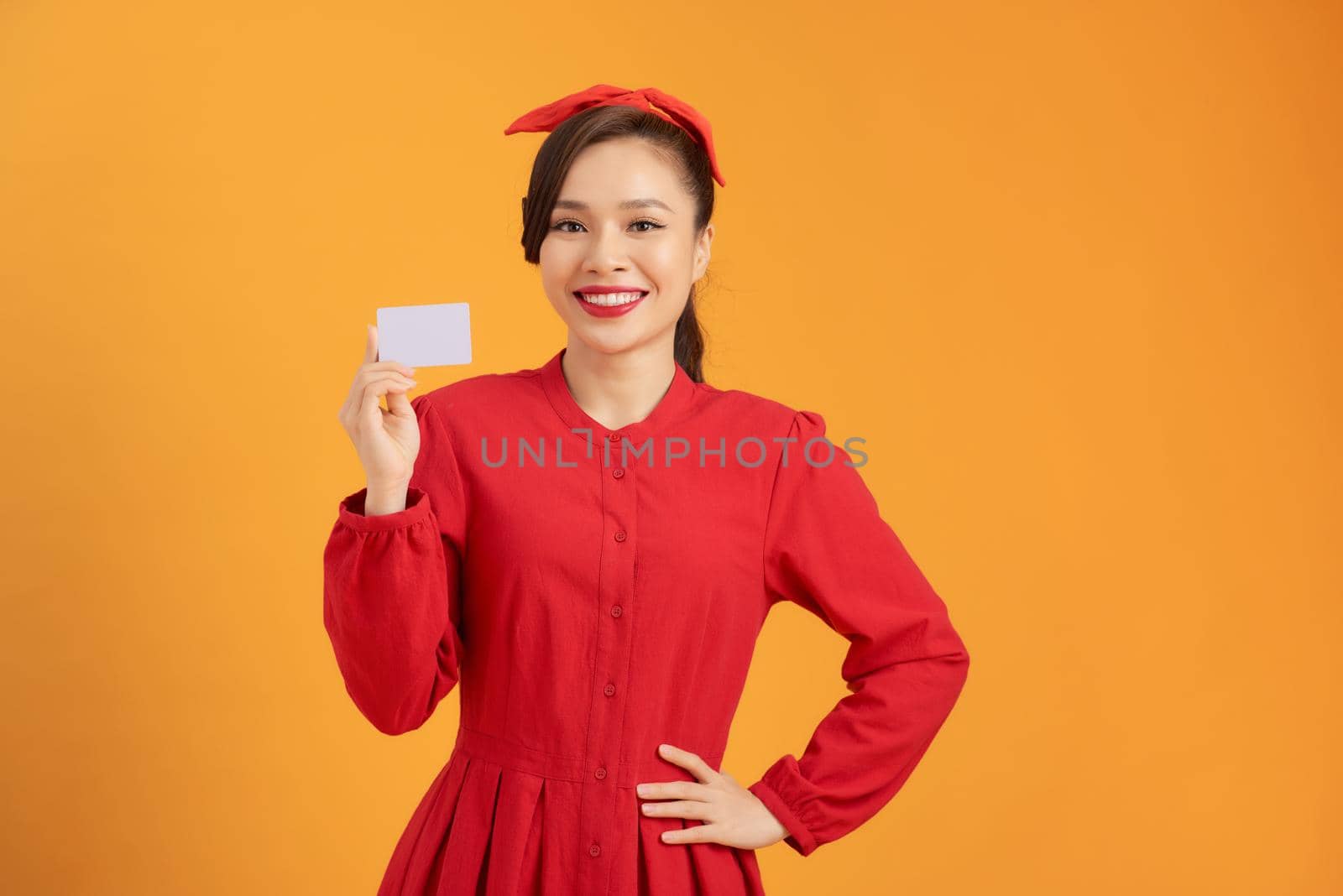 Young beautiful Asian woman holding credit card over orange isolated background 