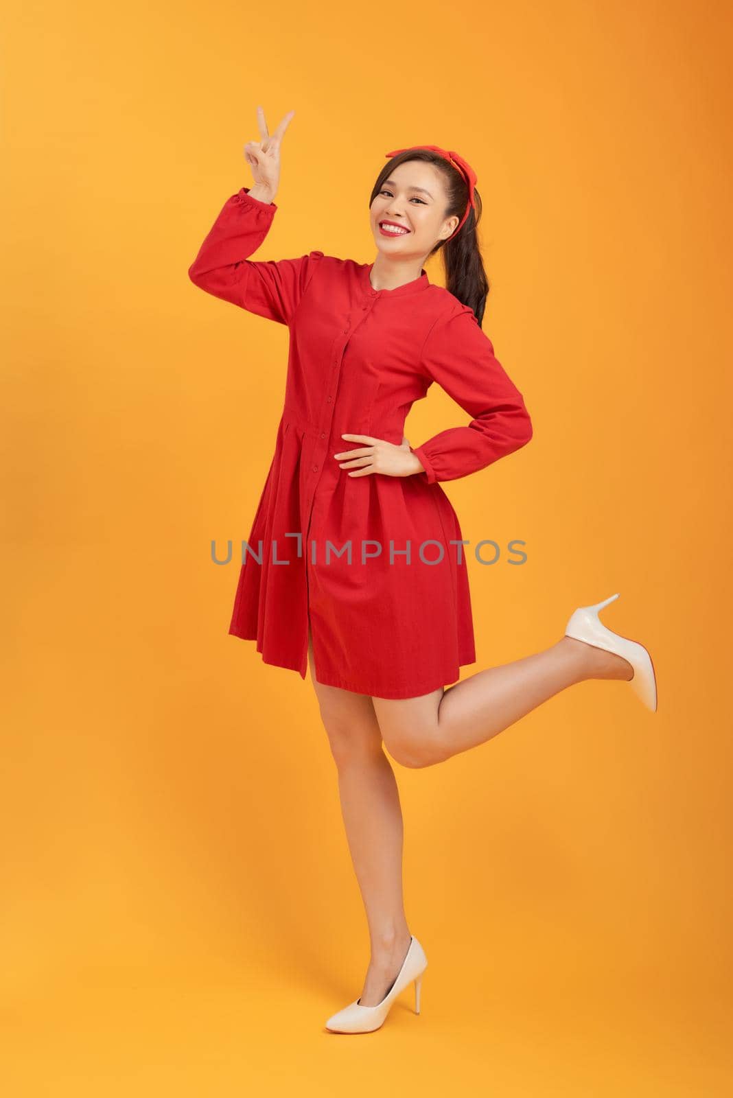 Young gorgoeus Asian woman in red dress standing over orange background. by makidotvn