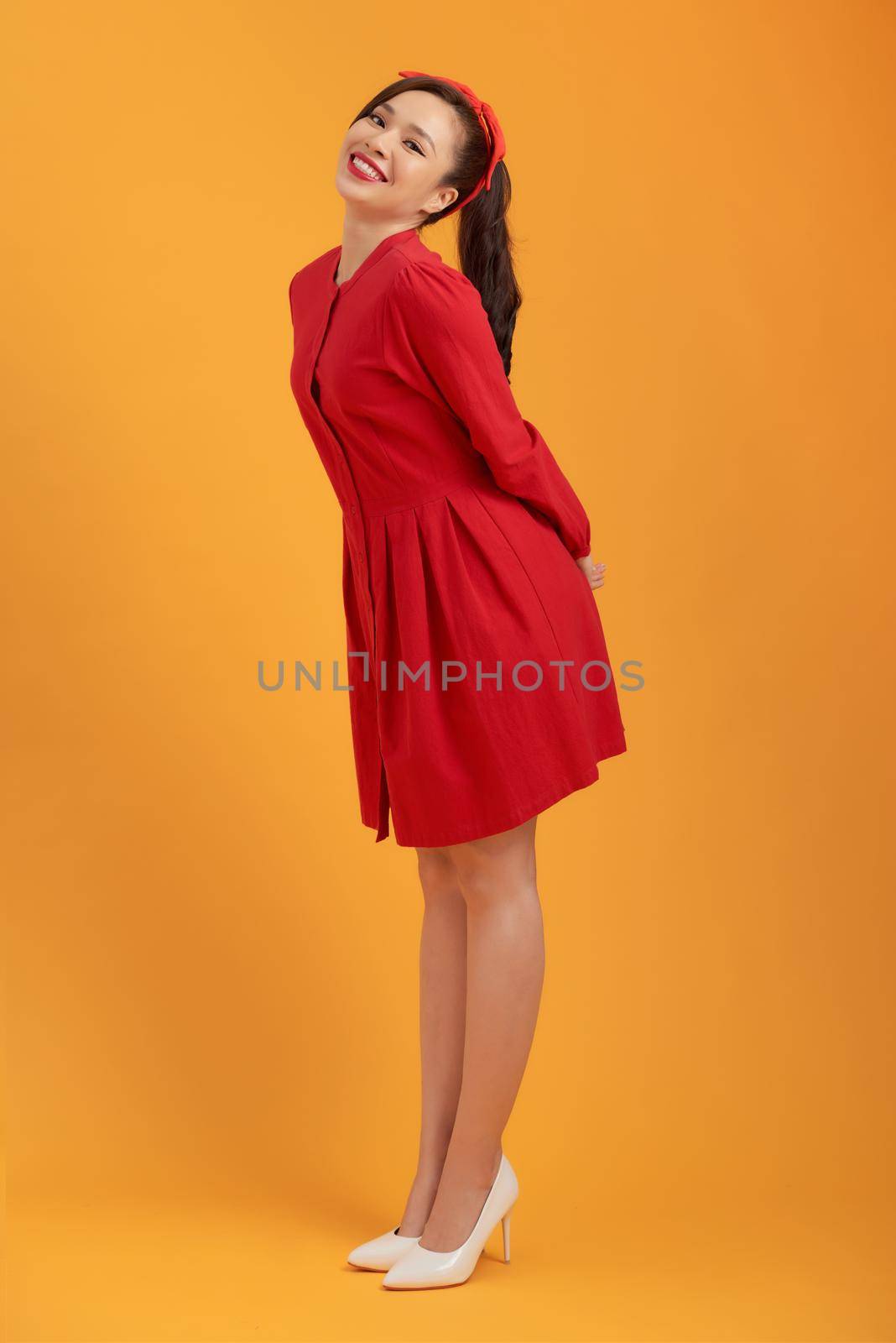 Beautiful lovely girl in red dress isolated on orange background in full body.