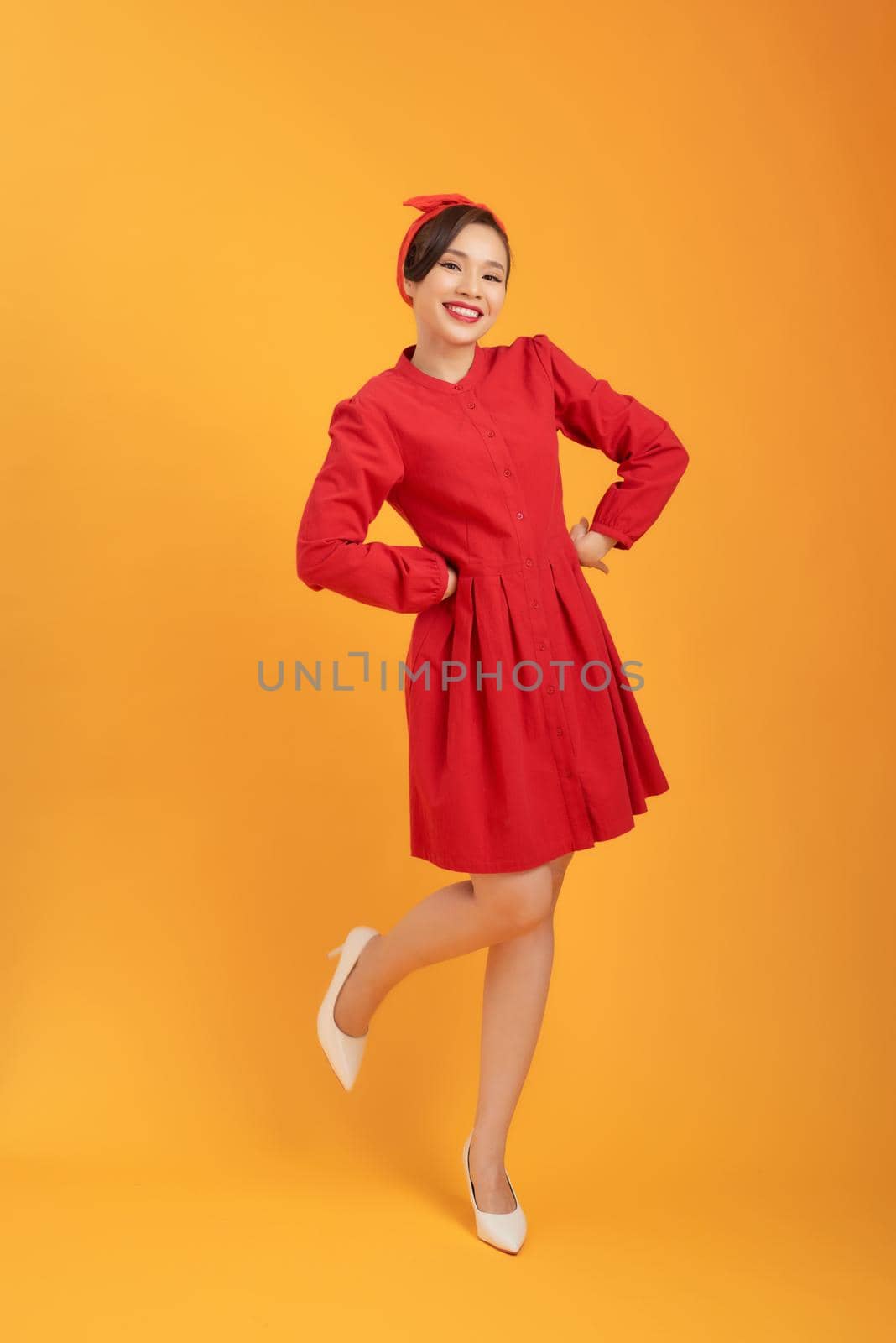 Young gorgoeus Asian woman in red dress standing over orange background.