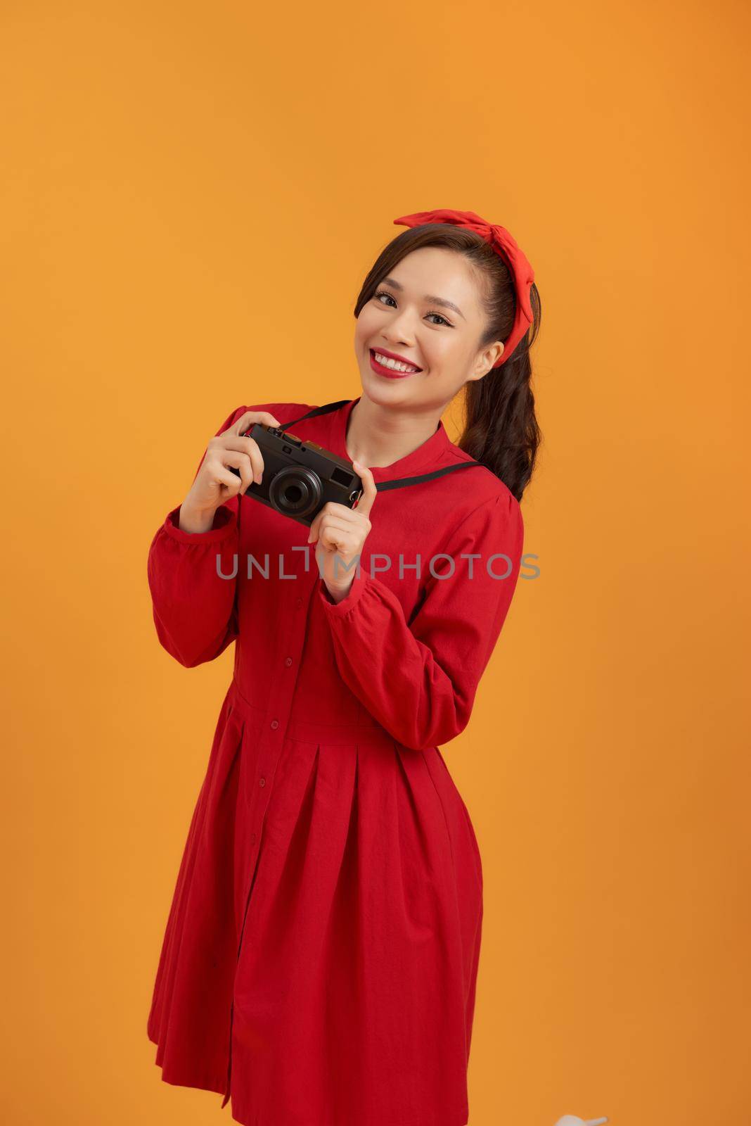 Young Asian woman with retro camera while standing isolated over orange background.